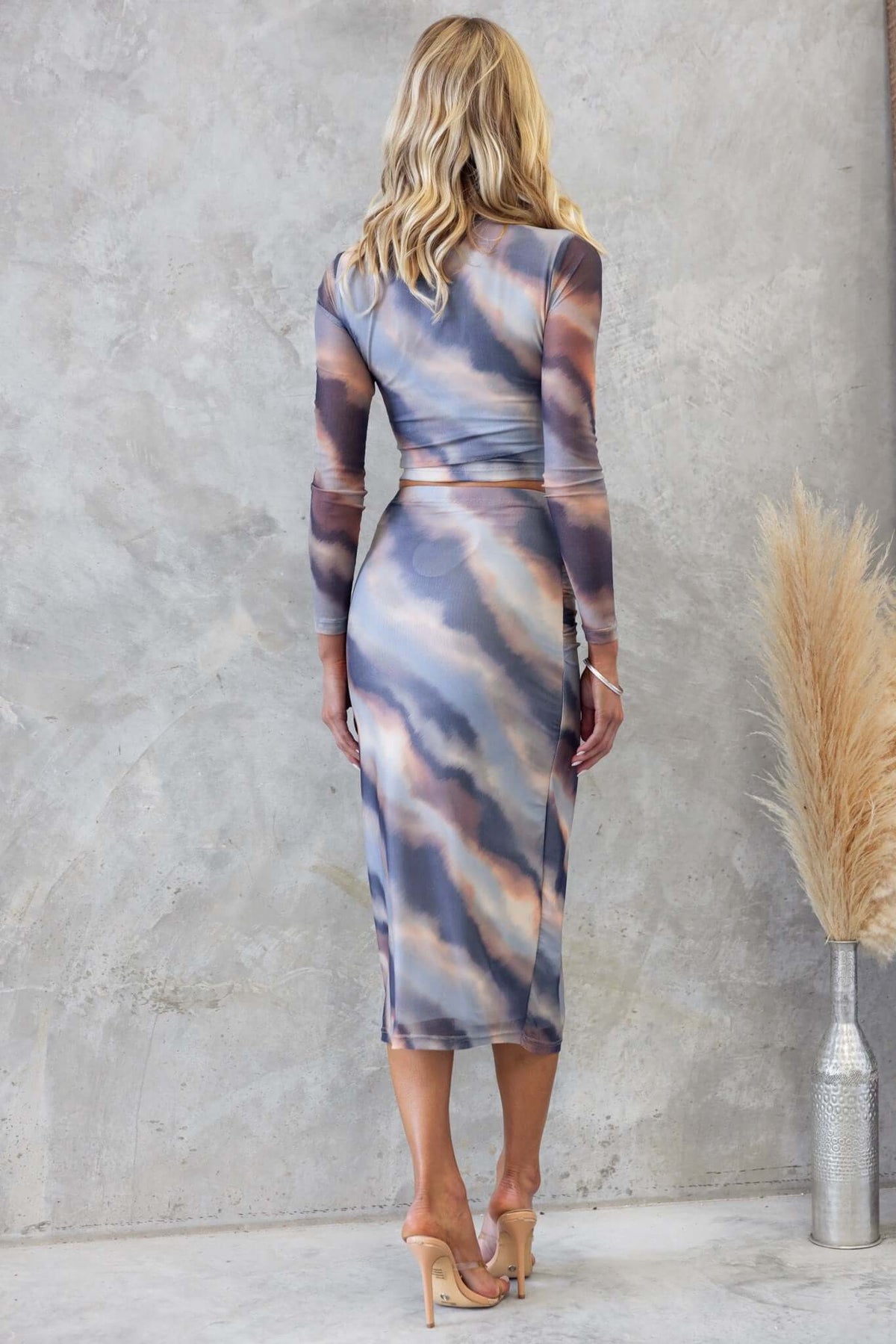 Back view of a woman in a stylish blue and brown wave-patterned midi dress, featuring a fitted silhouette and long sleeves.