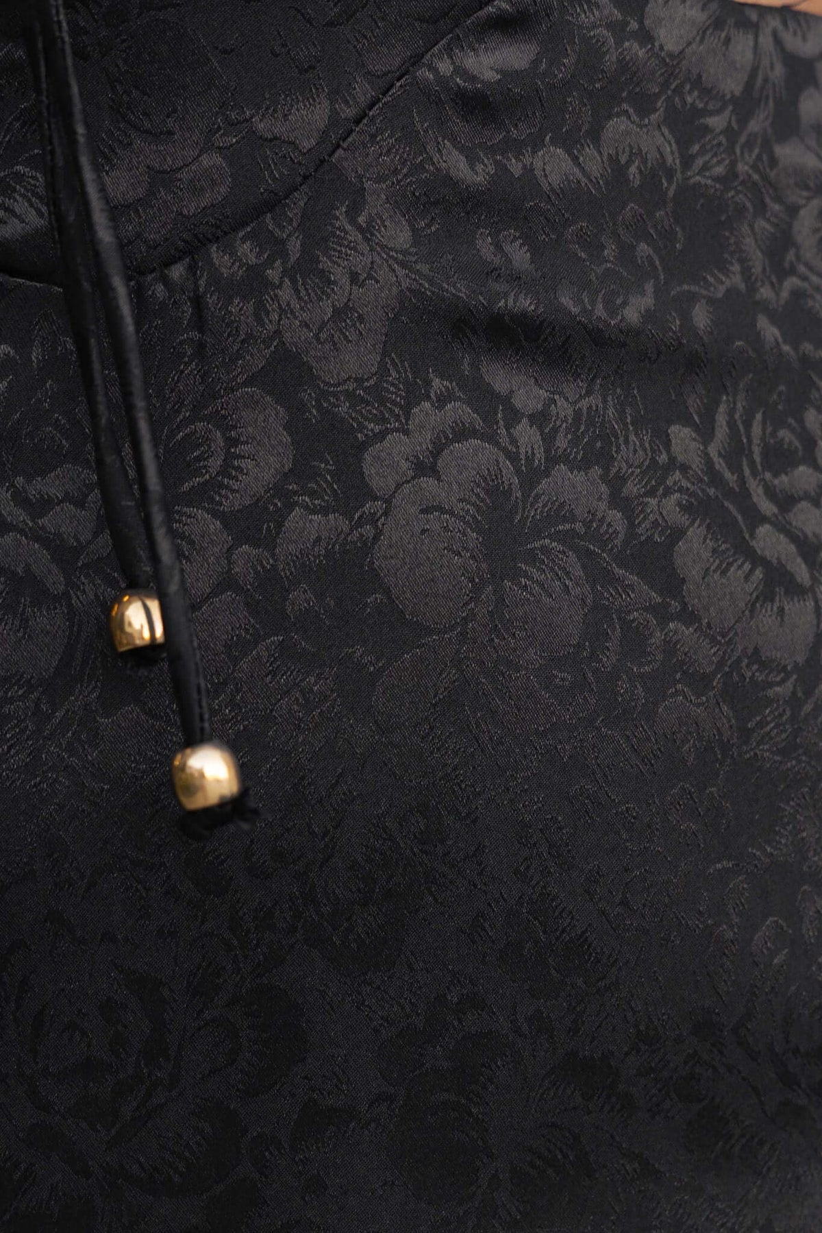 Close-up of the Dalma Dress showcasing elegant black fabric with floral pattern and decorative gold tie details.