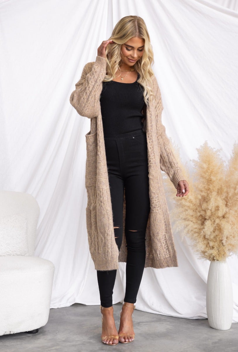 Emerson Cardigan featuring a cable knit style, longline fit, and pockets, worn with black pants and heels.
