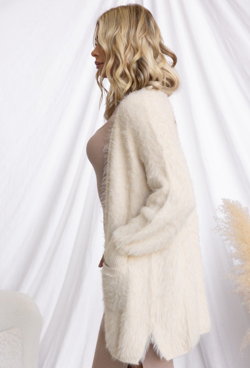 Side view of a woman wearing a fluffy white Erina Cardigan, featuring a relaxed fit and small side splits.