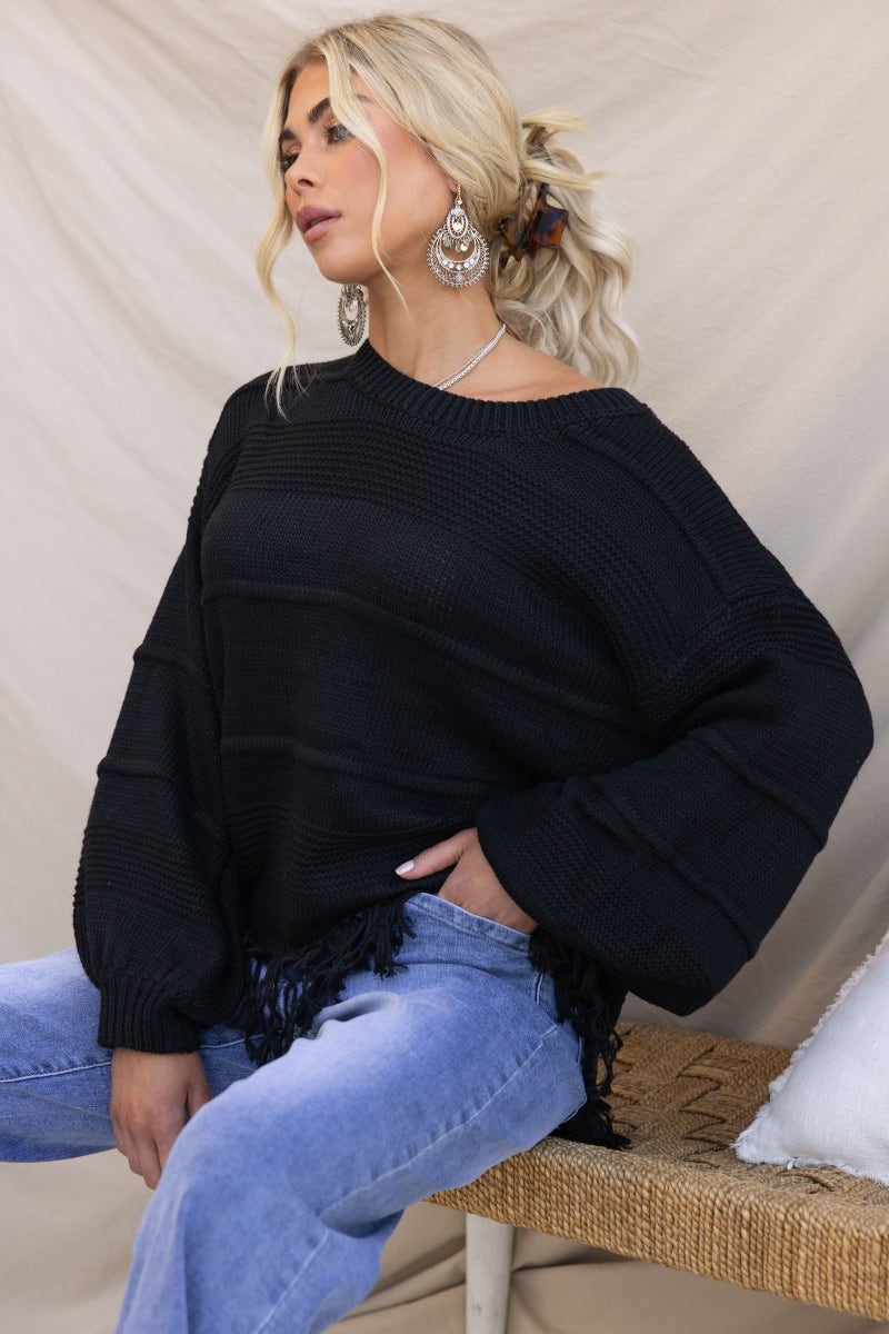 Model wearing Adela Knit black jumper with round neckline and tassle detail, styled with casual jeans.