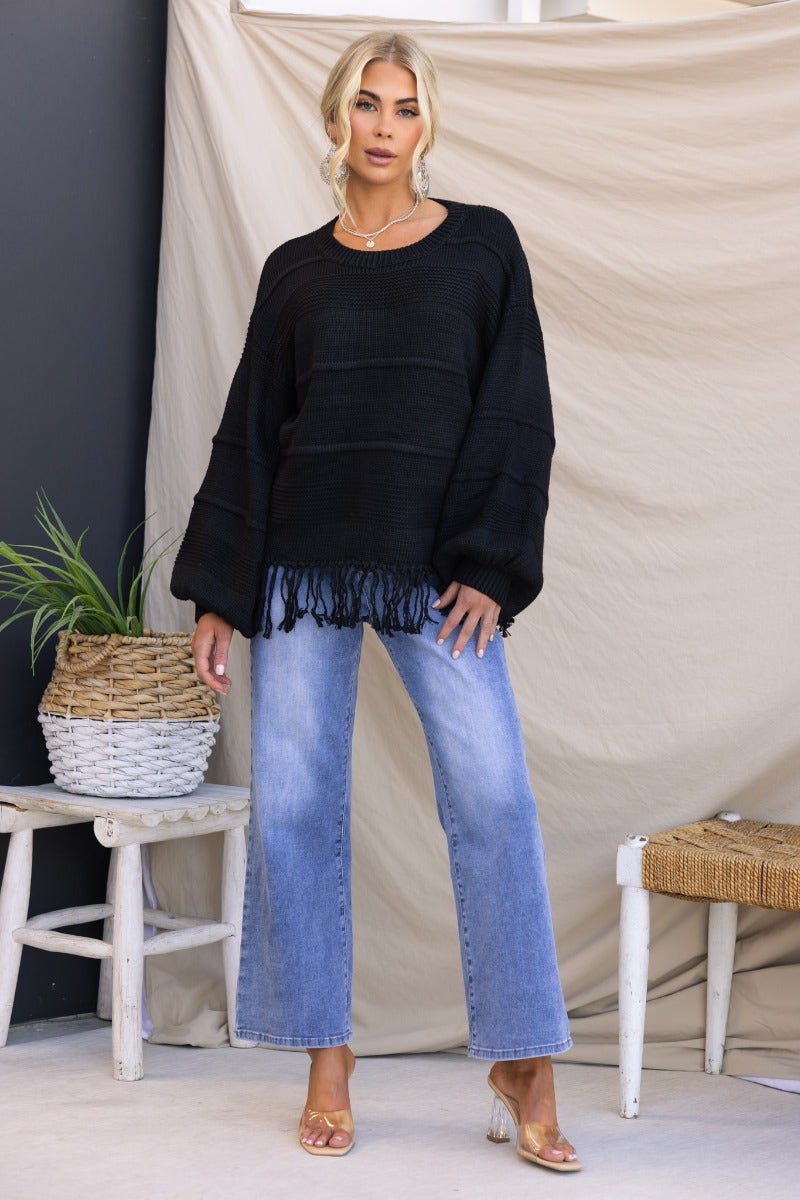 Model wearing a black knit jumper with tassle detail, paired with light blue jeans, showcasing a relaxed fit.