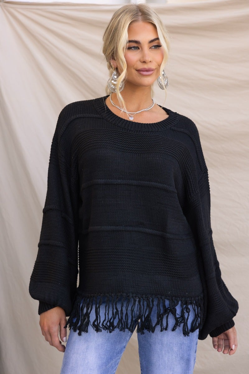 Black knit jumper with tassel detail, round neckline, worn by model with relaxed fit.