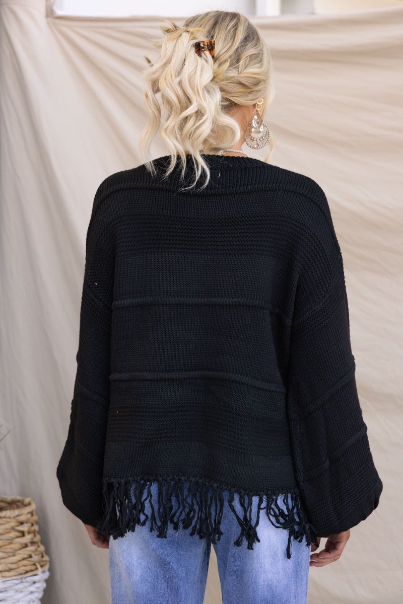 Back view of Adela Knit black jumper with tassle detail, styled with relaxed jeans and a casual braid hairstyle.