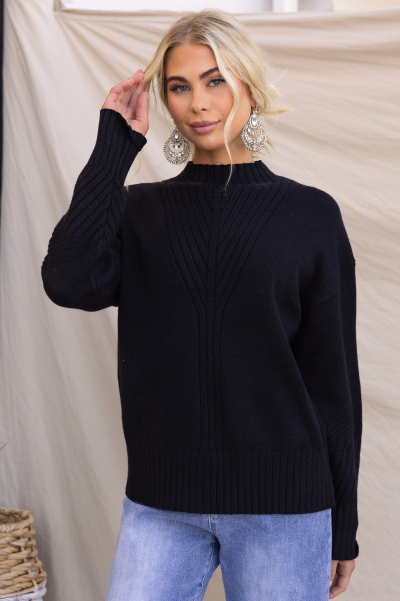Black ribbed knit Cuba jumper with mock neckline, styled with relaxed fit and worn by model with earrings.