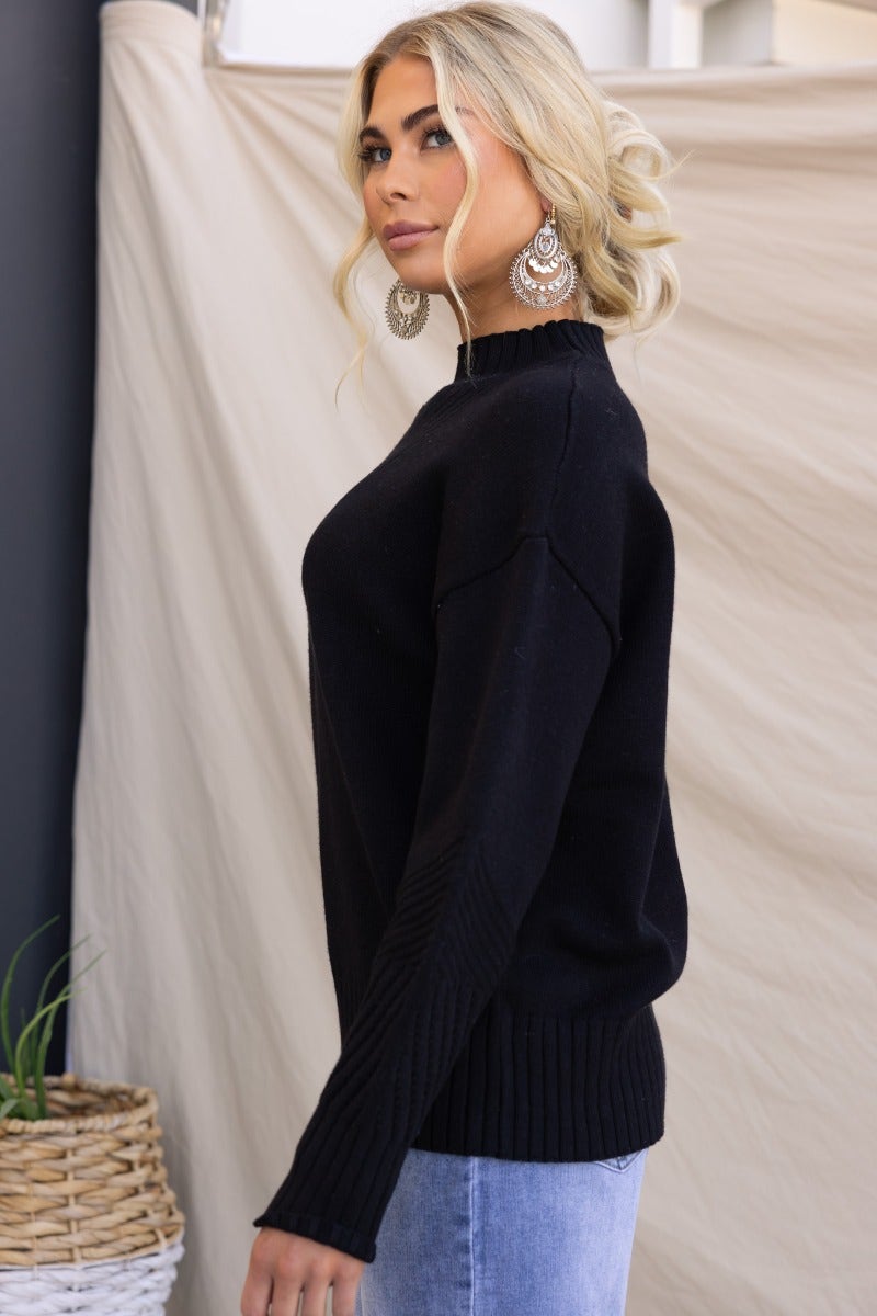 Model wearing a black ribbed knit Cuba Jumper with mock neckline, styled with earrings against a neutral backdrop.