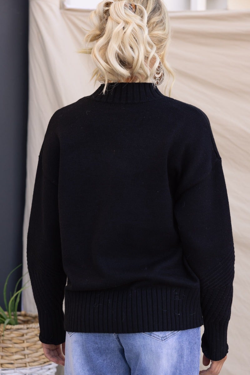 Back view of Cuba Jumper in black ribbed knit, featuring mock neckline and relaxed fit, styled with jeans.