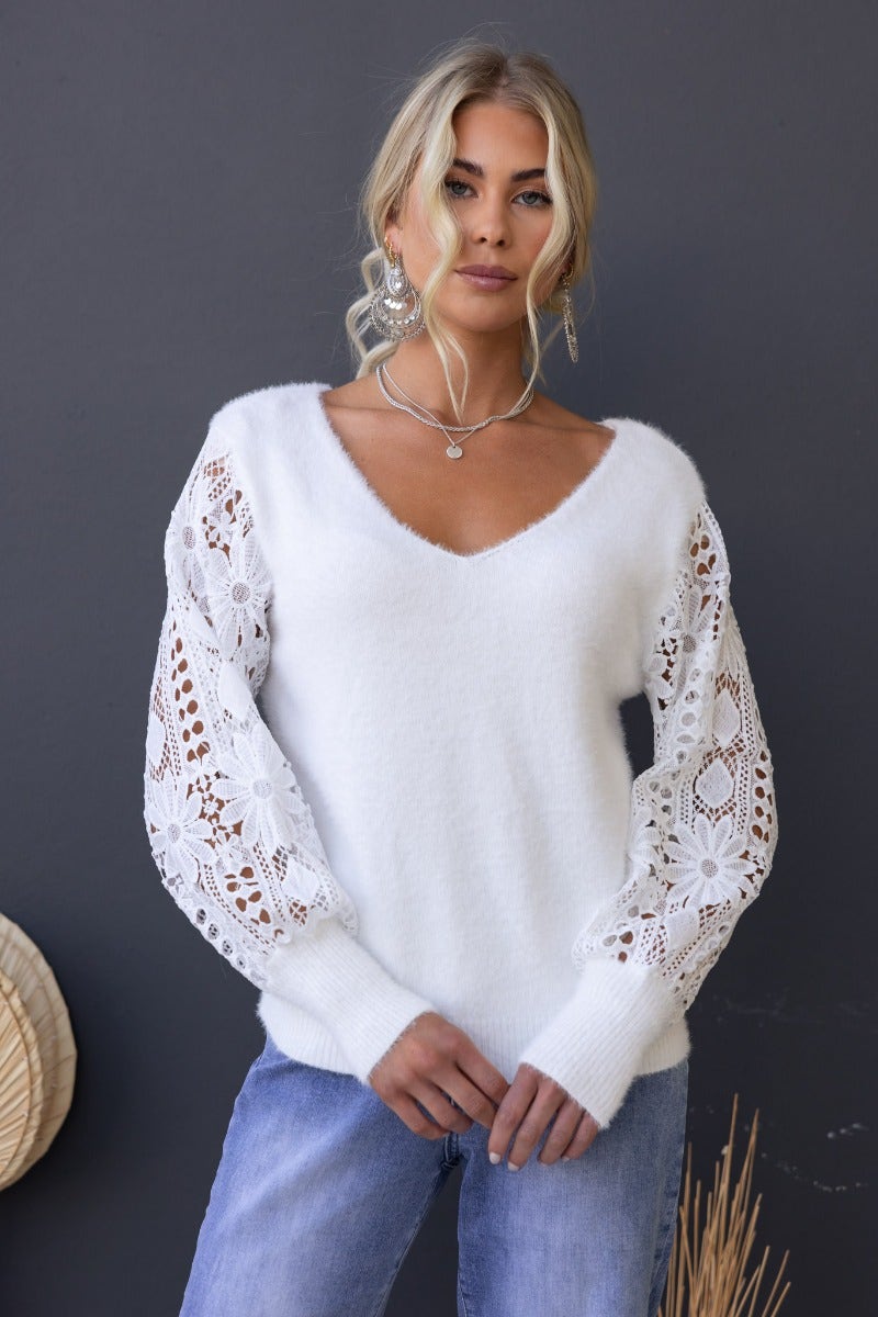 Fluffy knit Indya jumper with V-neckline and lace sleeves, modeled by woman in white against dark background.