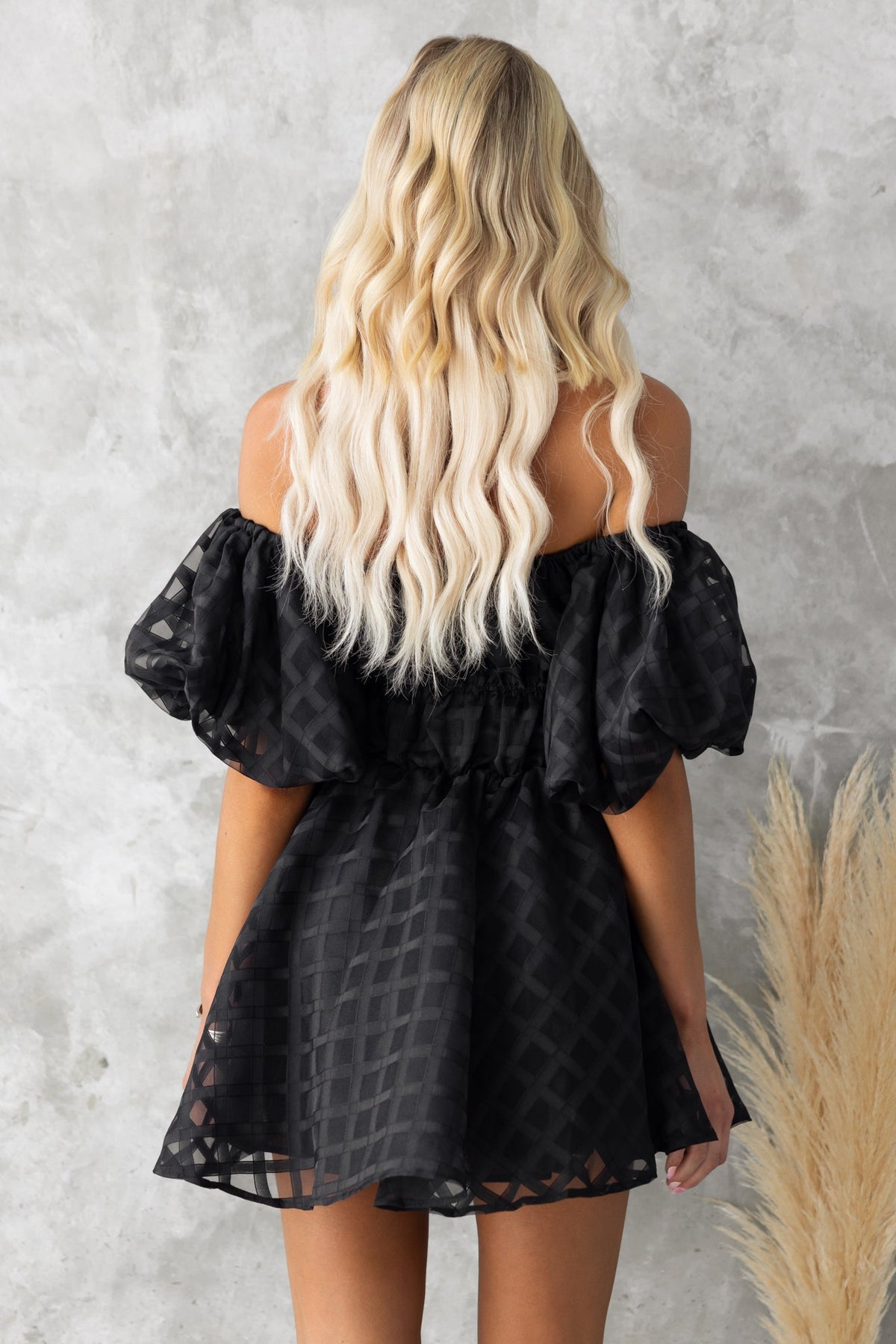 Back view of Zerali black off-shoulder dress with puff sleeves and elastic neckline against a textured background.