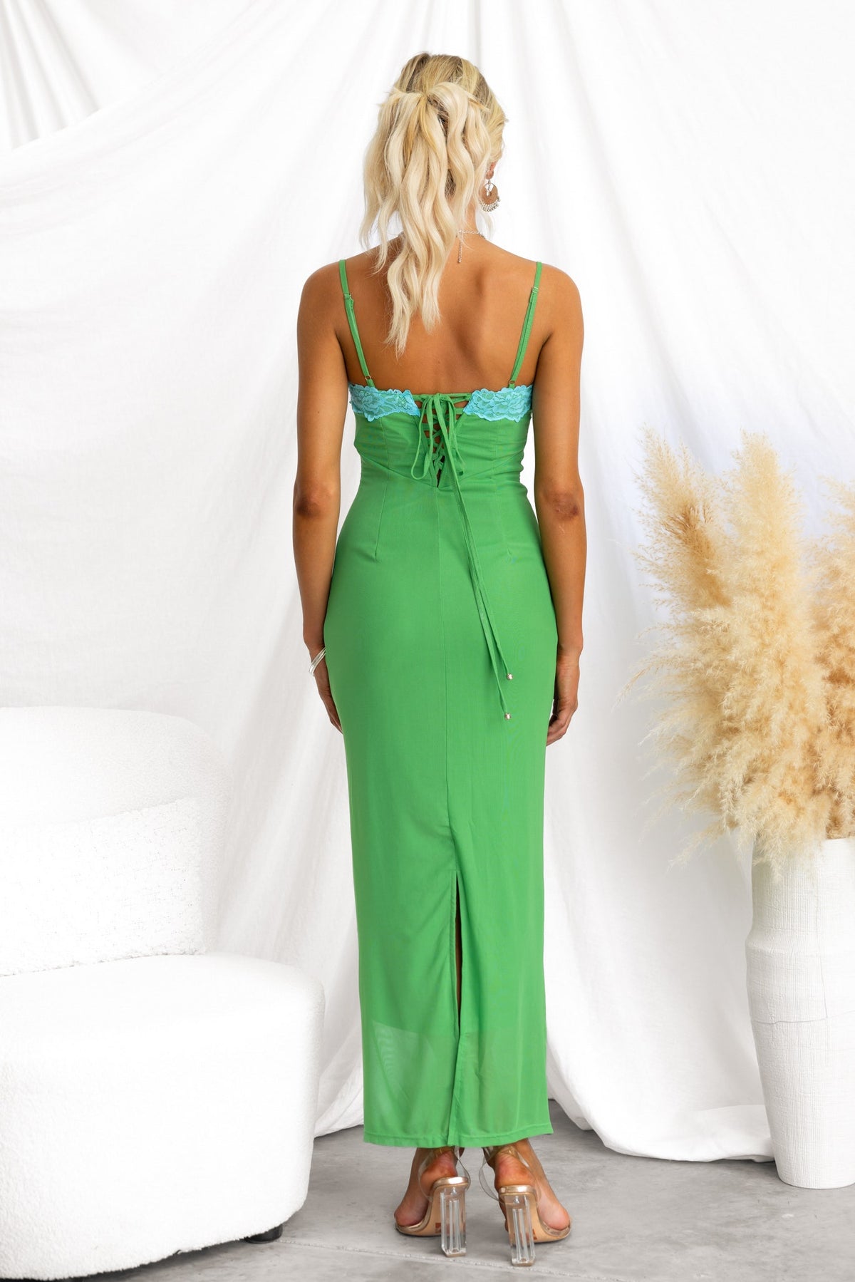 Back view of a model in a green bodycon maxi dress with lace-up tie, adjustable straps, and split hem.