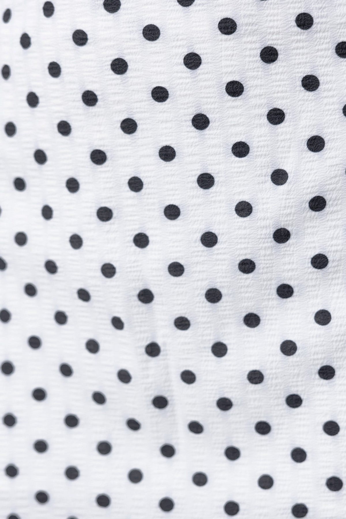 Close-up of white fabric with black polka dots, highlighting the texture for the Cruella Top.