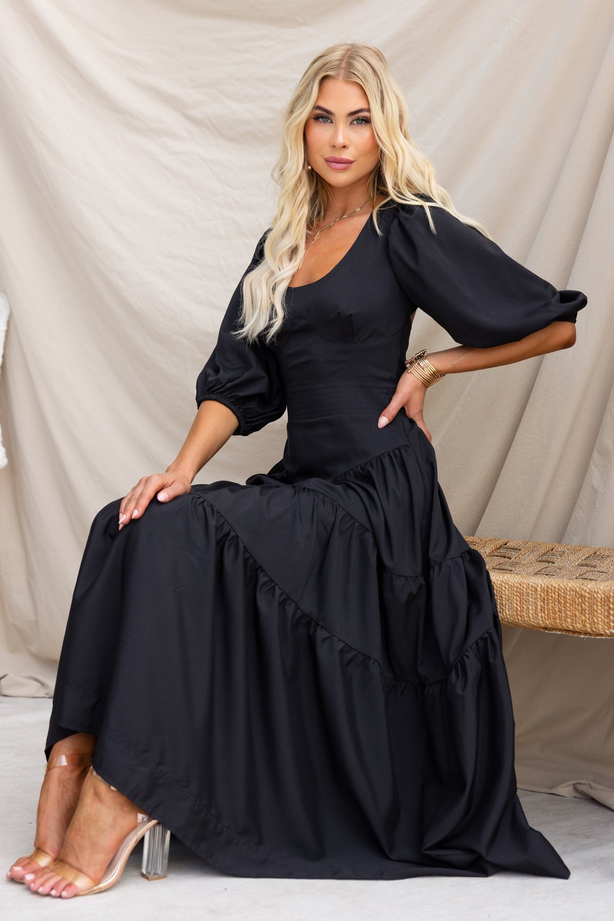 Elegant black midi dress with puff sleeves, round neckline, and tiered design, shown by model in relaxed pose.