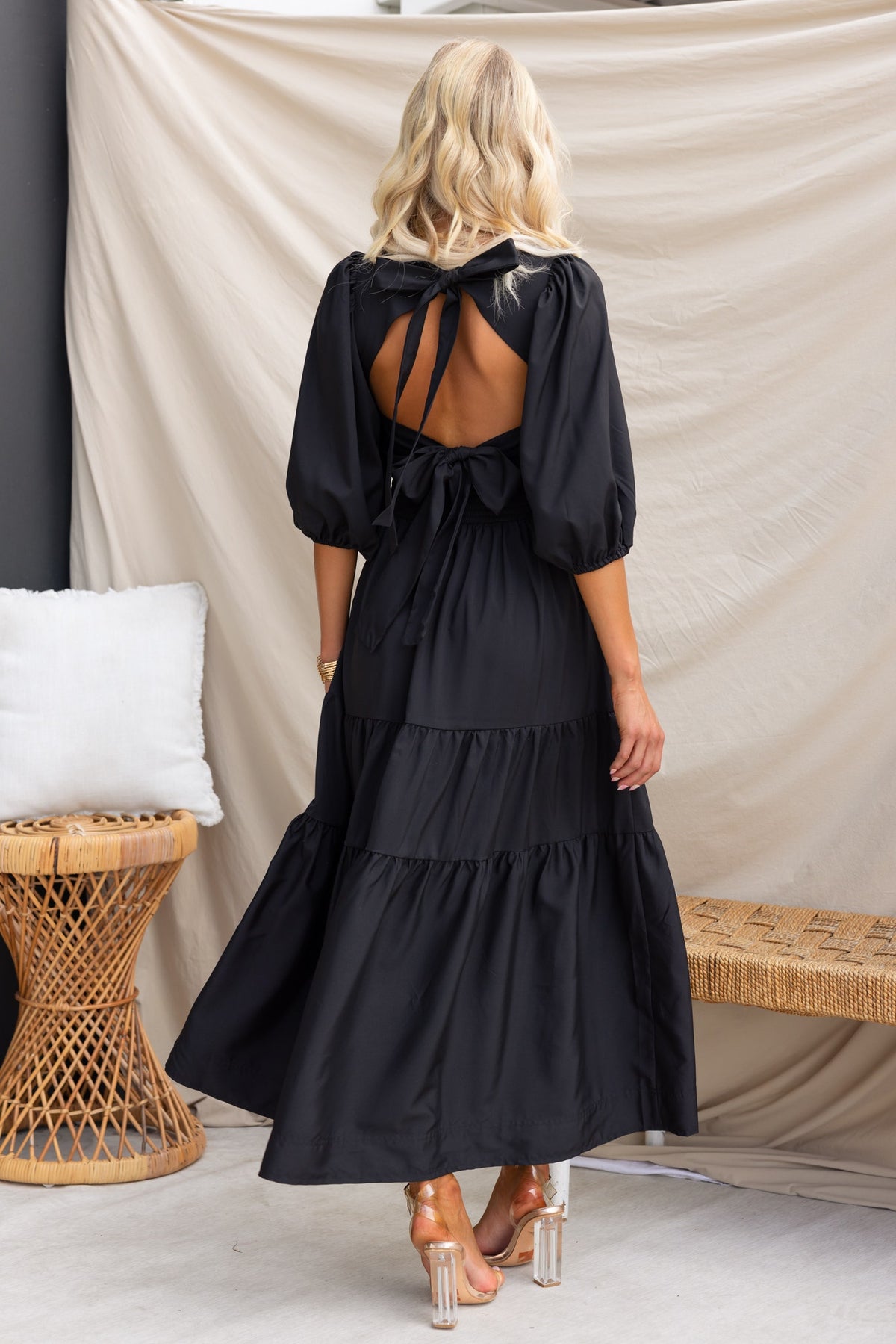 Back view of a model wearing a black Merle Midi Dress with puff sleeves and a tie detail.