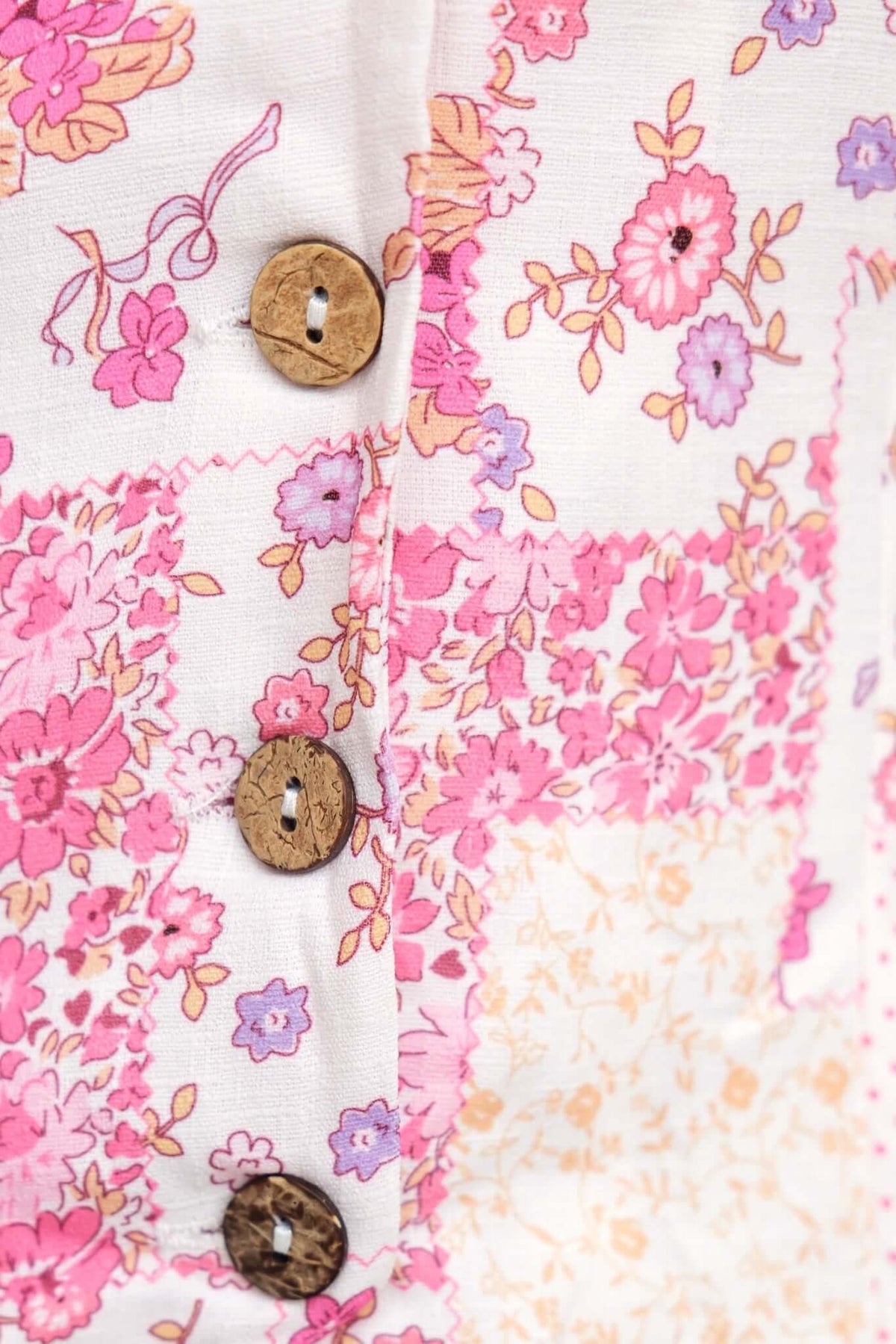 Close-up of floral patterned fabric with wooden buttons on the Rewn Playsuit, showcasing vibrant pinks and soft hues.