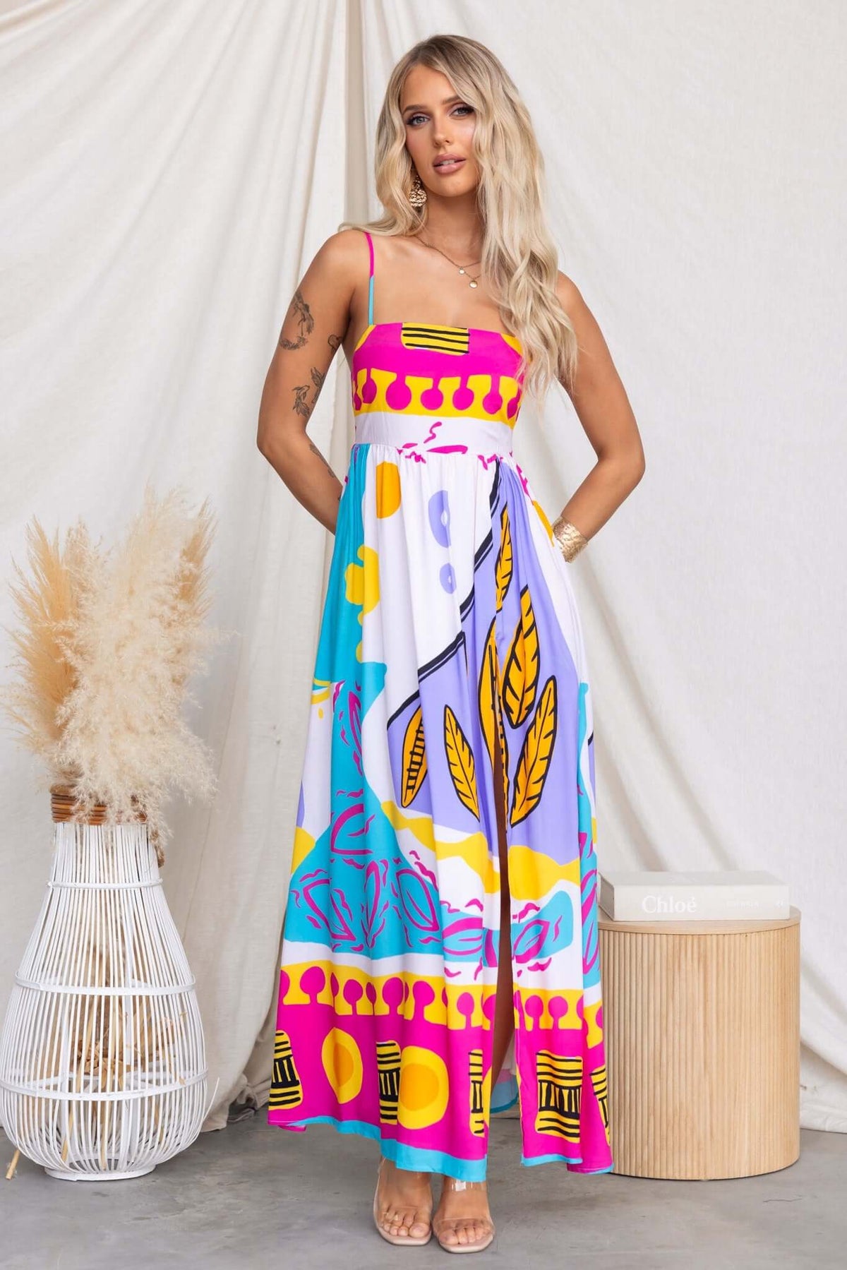 Orella Maxi Dress featuring colorful print, adjustable straps, and high split, styled with a natural background.