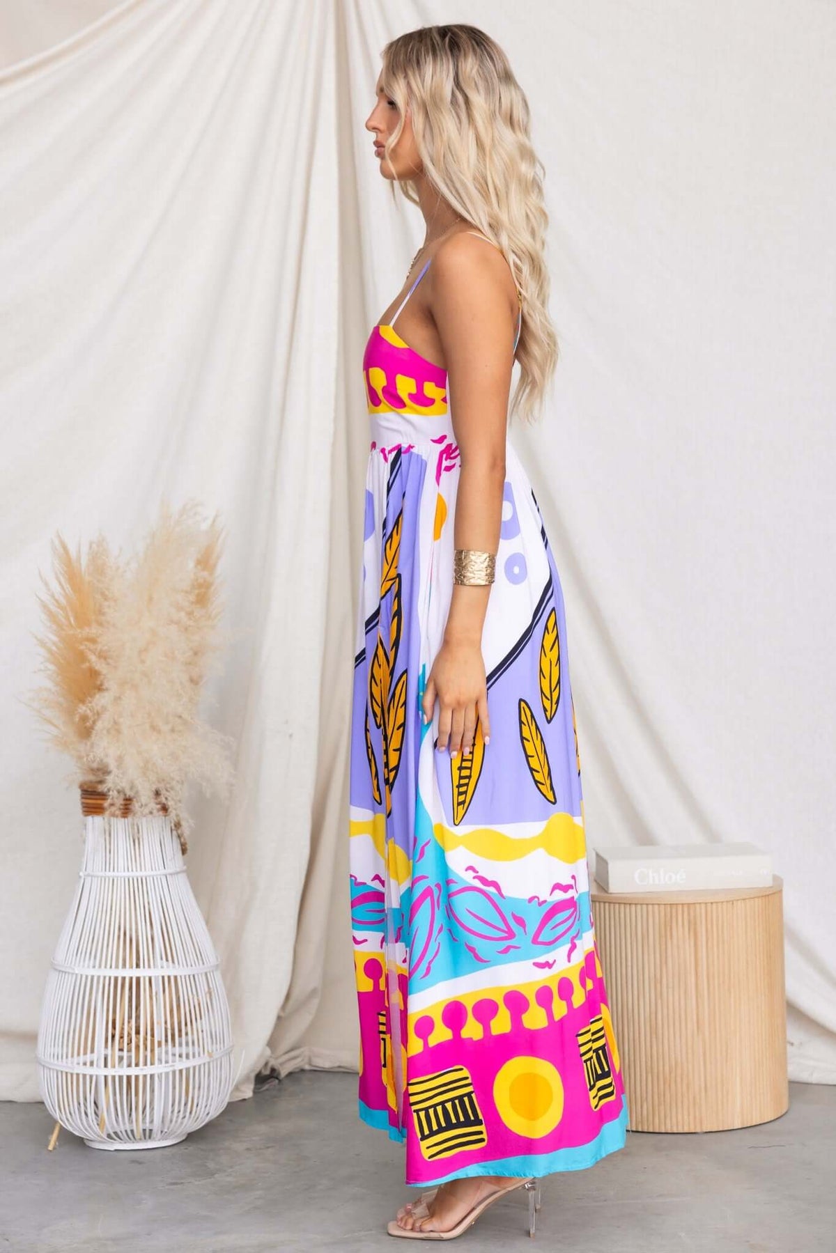 Model in stylish Orella Maxi Dress with adjustable straps, vibrant print, and high front split, shown in a chic setting.