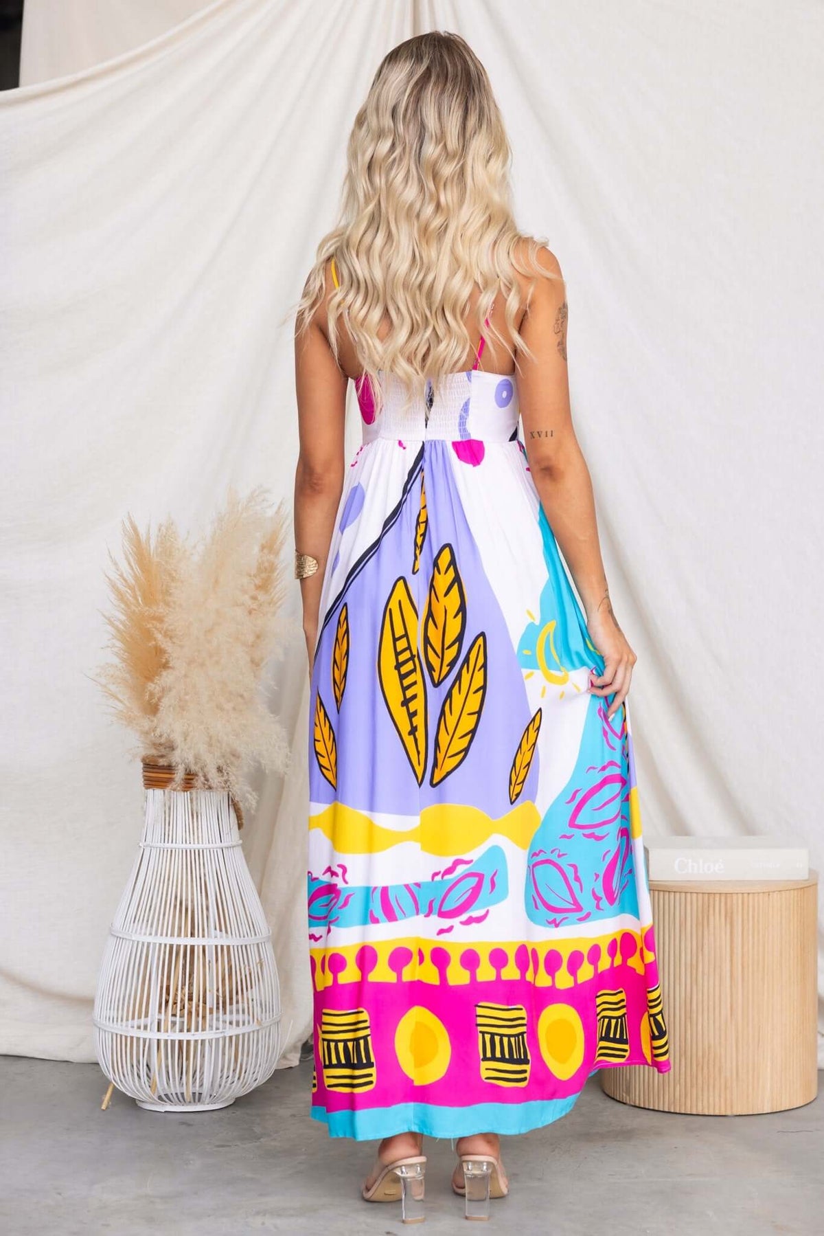 Back view of a woman in a vibrant printed Orella maxi dress with adjustable straps and a high front split.