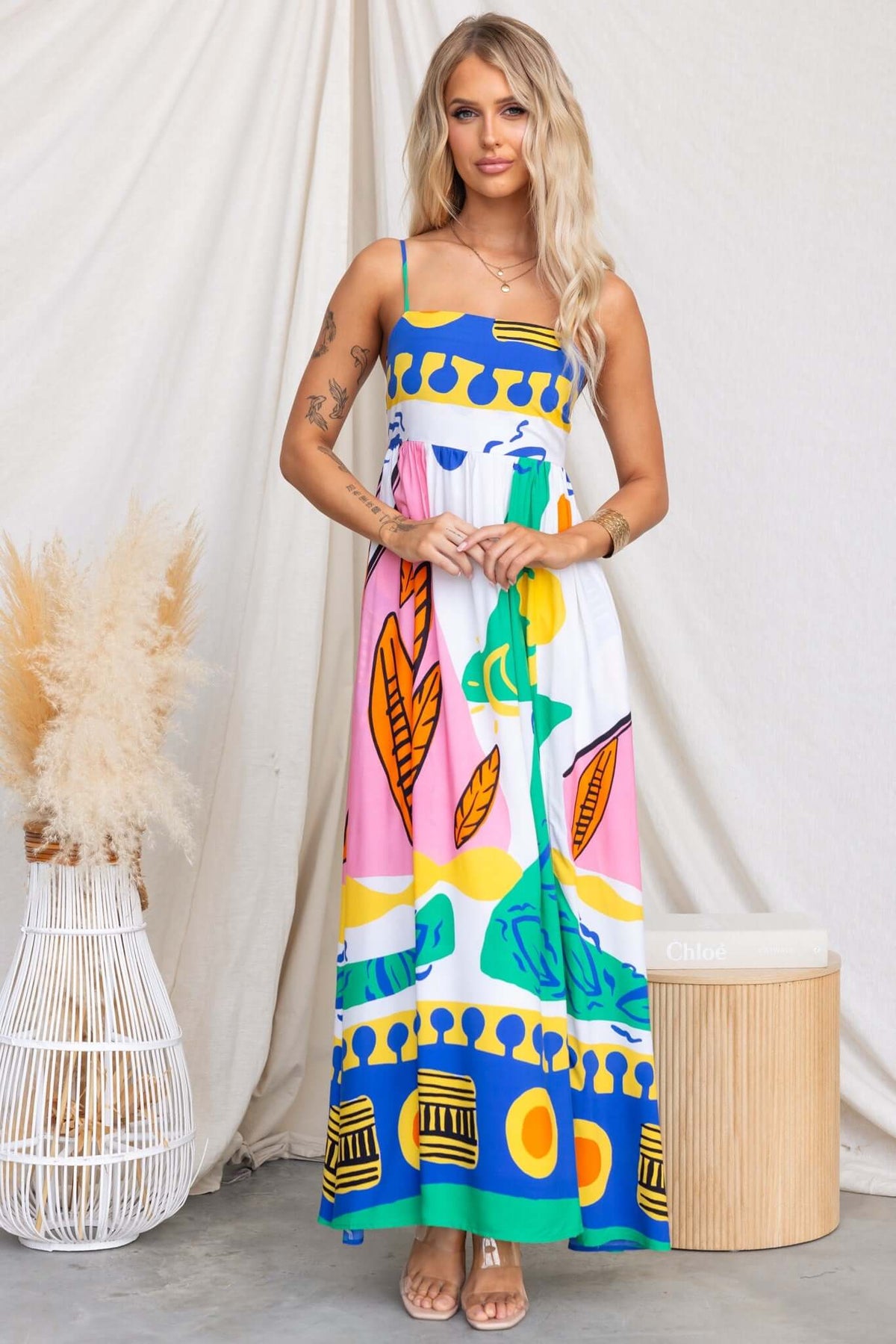 Orella Maxi Dress with colorful print, adjustable straps, and pockets, displayed on model in bright, summery setting.