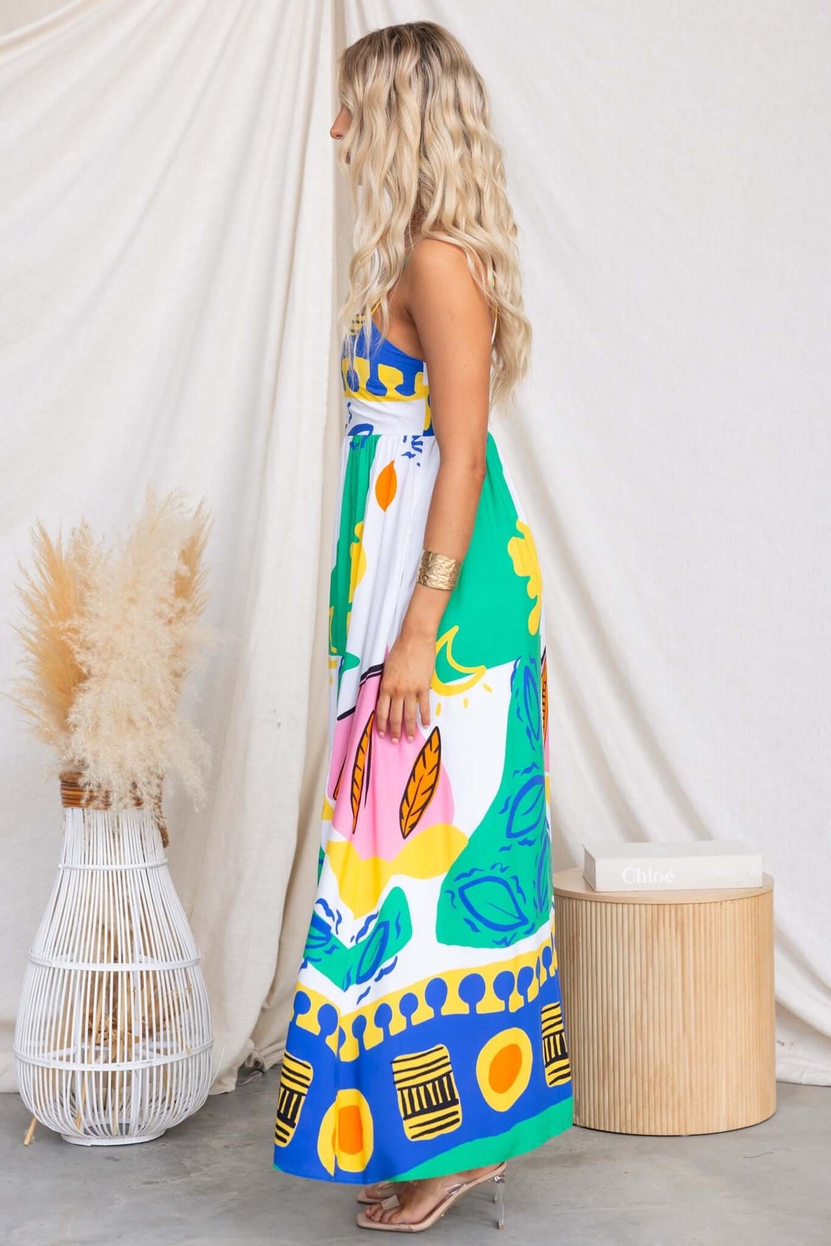 Side view of a model wearing the Orella Maxi Dress, featuring vibrant colors and a high split, accessorized elegantly.