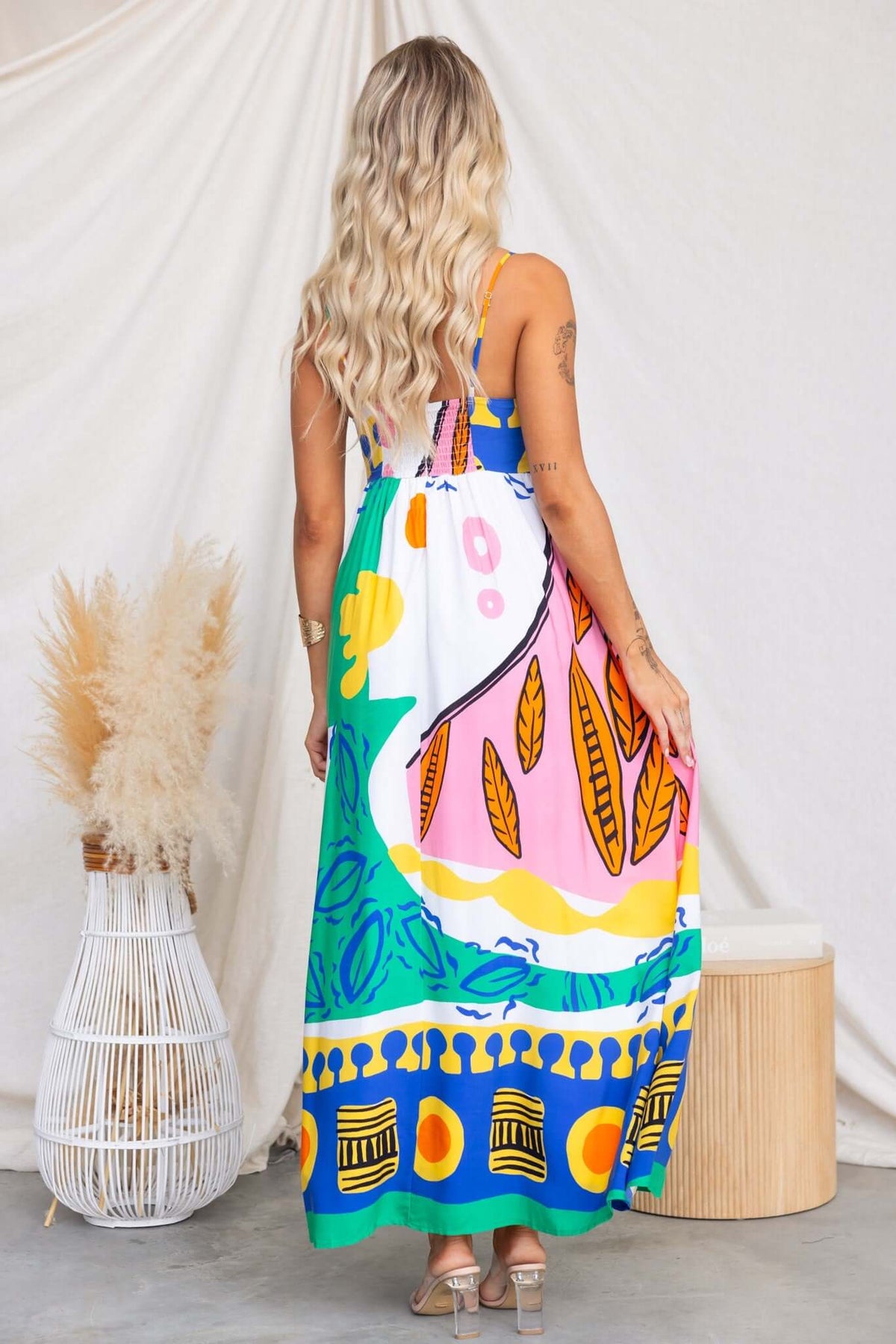 Back view of a colorful Orella Maxi Dress with adjustable straps and high split, featuring a lively print and pockets.