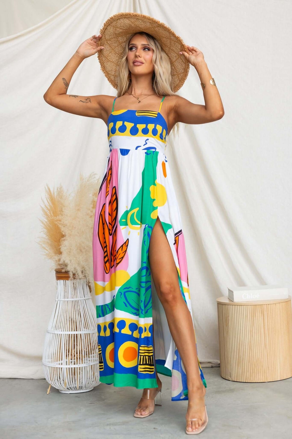 Model in colorful Orella Maxi Dress with adjustable straps and high split, accessorized with a straw hat.
