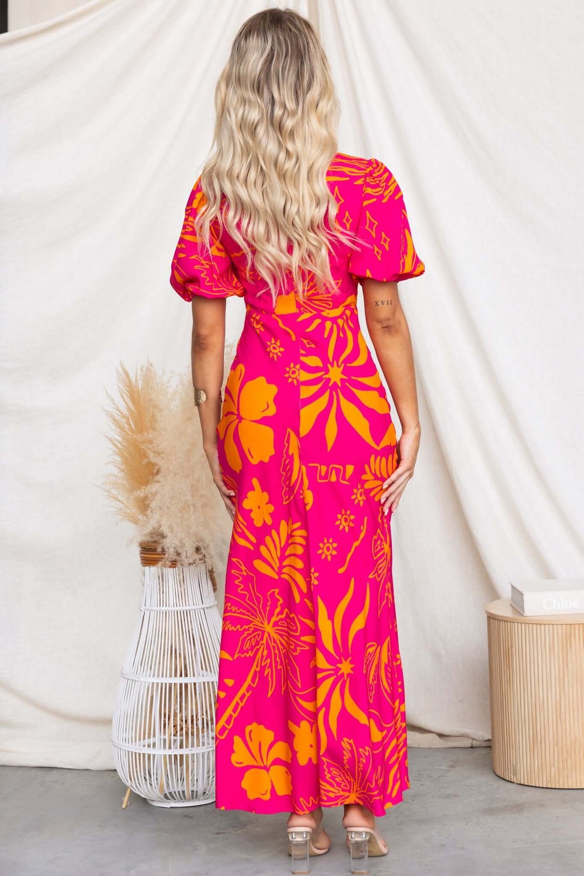 Model wearing Nowah Maxi Dress in vibrant pink floral print, showcasing the back view with puff sleeves and elegant design.