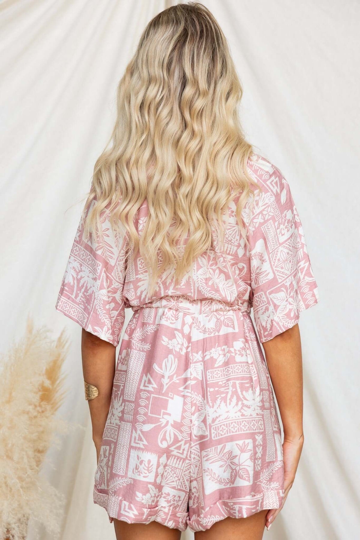 Back view of a Huxley Playsuit in pink pattern, featuring relaxed fit, elastic waistband, and short sleeves.