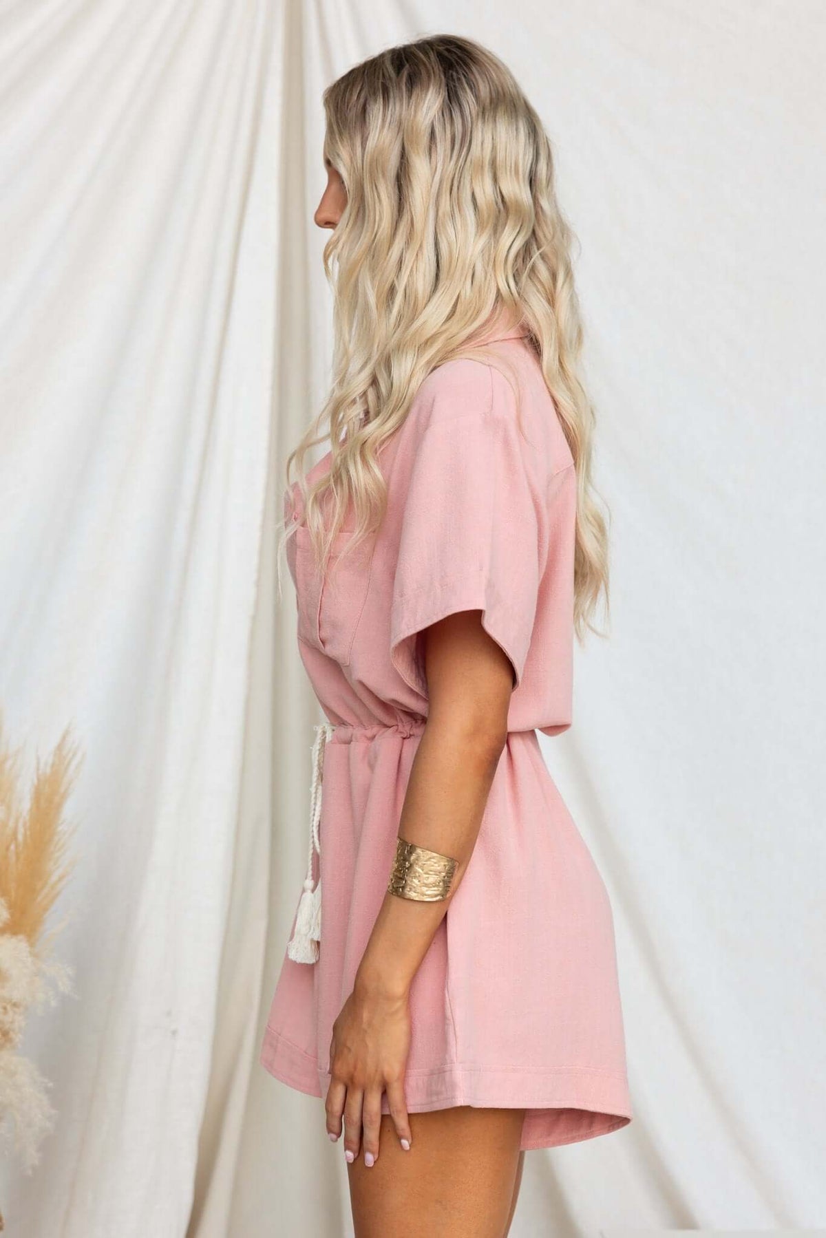 Woman in a pink Barre playsuit featuring a collar, button-up front, and drawstring waist, perfect for casual wear.