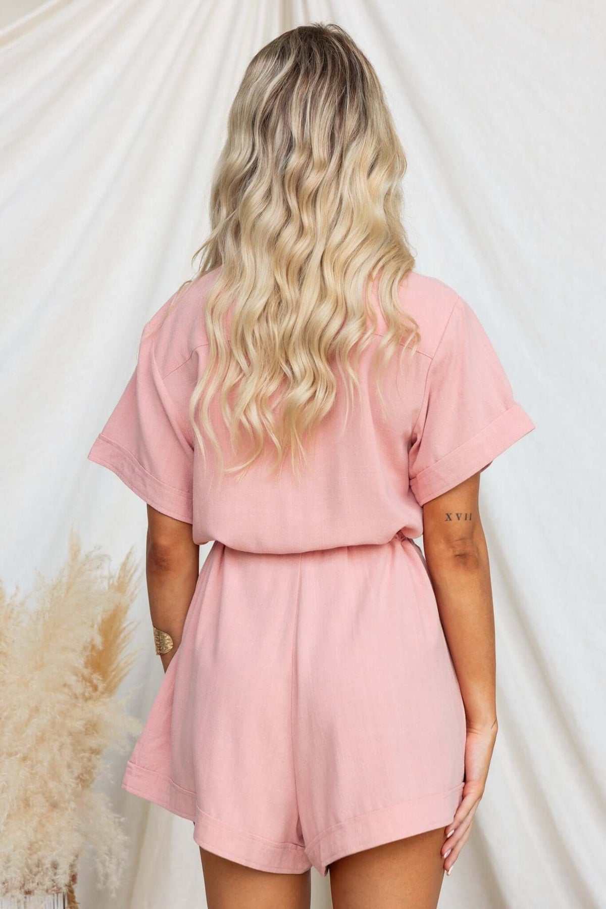 Back view of a model wearing a pink Barre Playsuit with a drawstring waist and short sleeves.