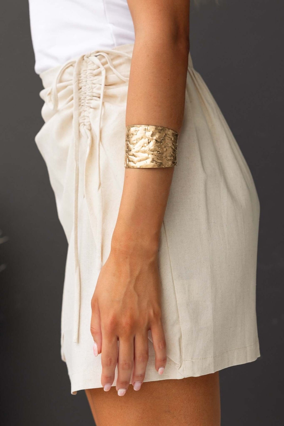 Side view of a model wearing the Quatro Skirt with a mid-high waist and tie front detail, featuring a gold bracelet.