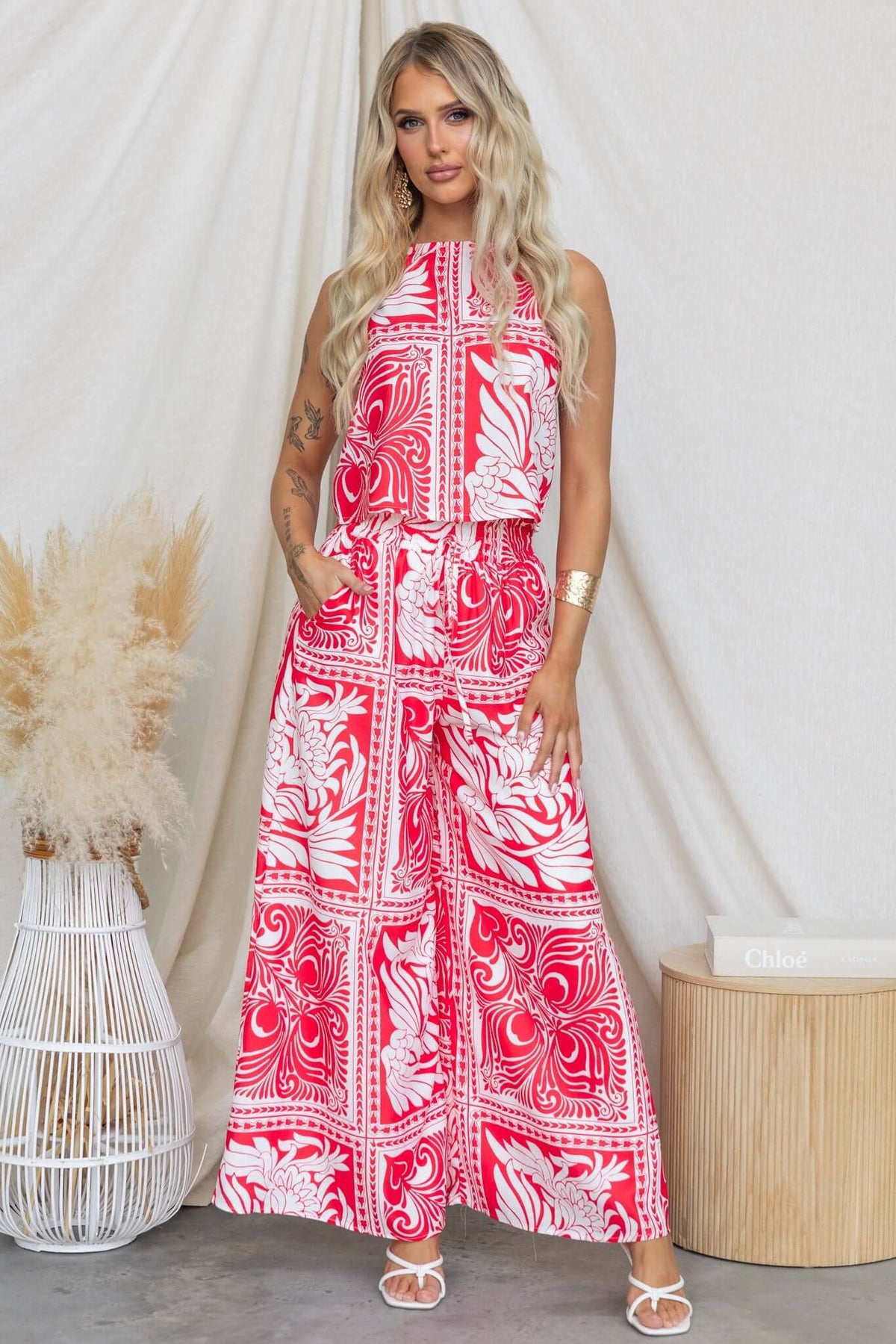 Model wearing a stylish red and white printed top and wide-leg pants outfit against a neutral backdrop.