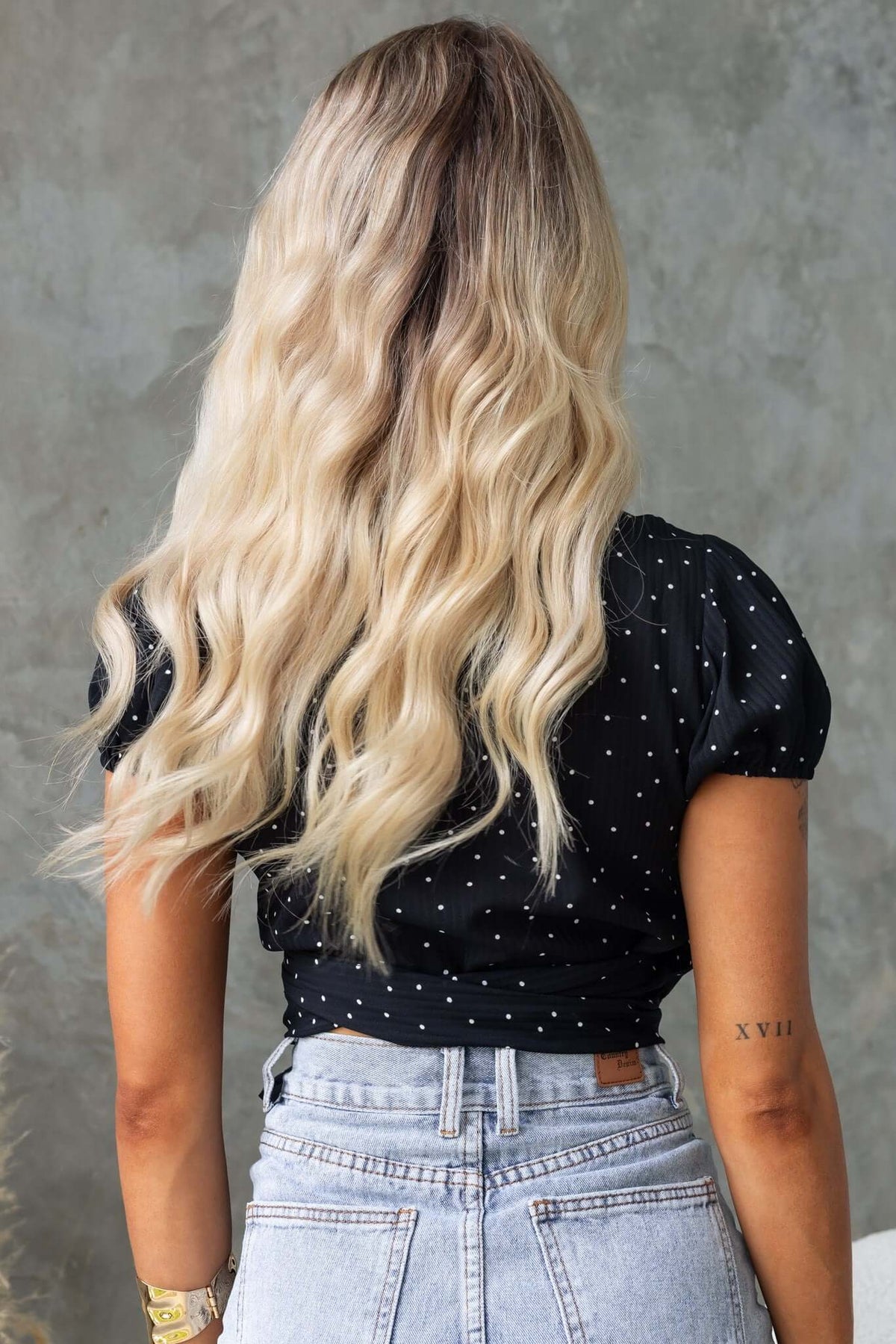 Back view of a woman in a black polka dot top with puff sleeves, styled with wavy blonde hair.