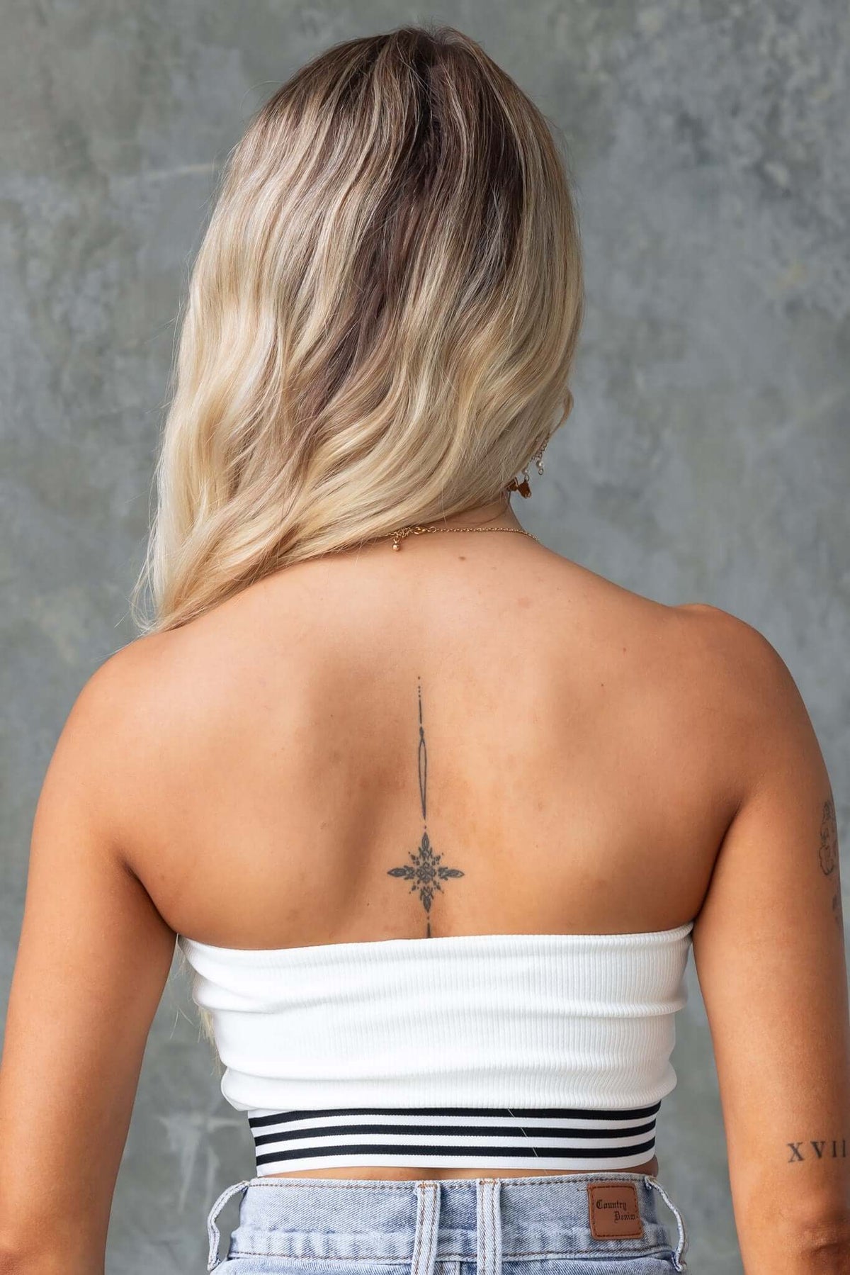 Back view of a woman wearing the Brice Top, a ribbed, elastic hem top with a stylish striped waistband.