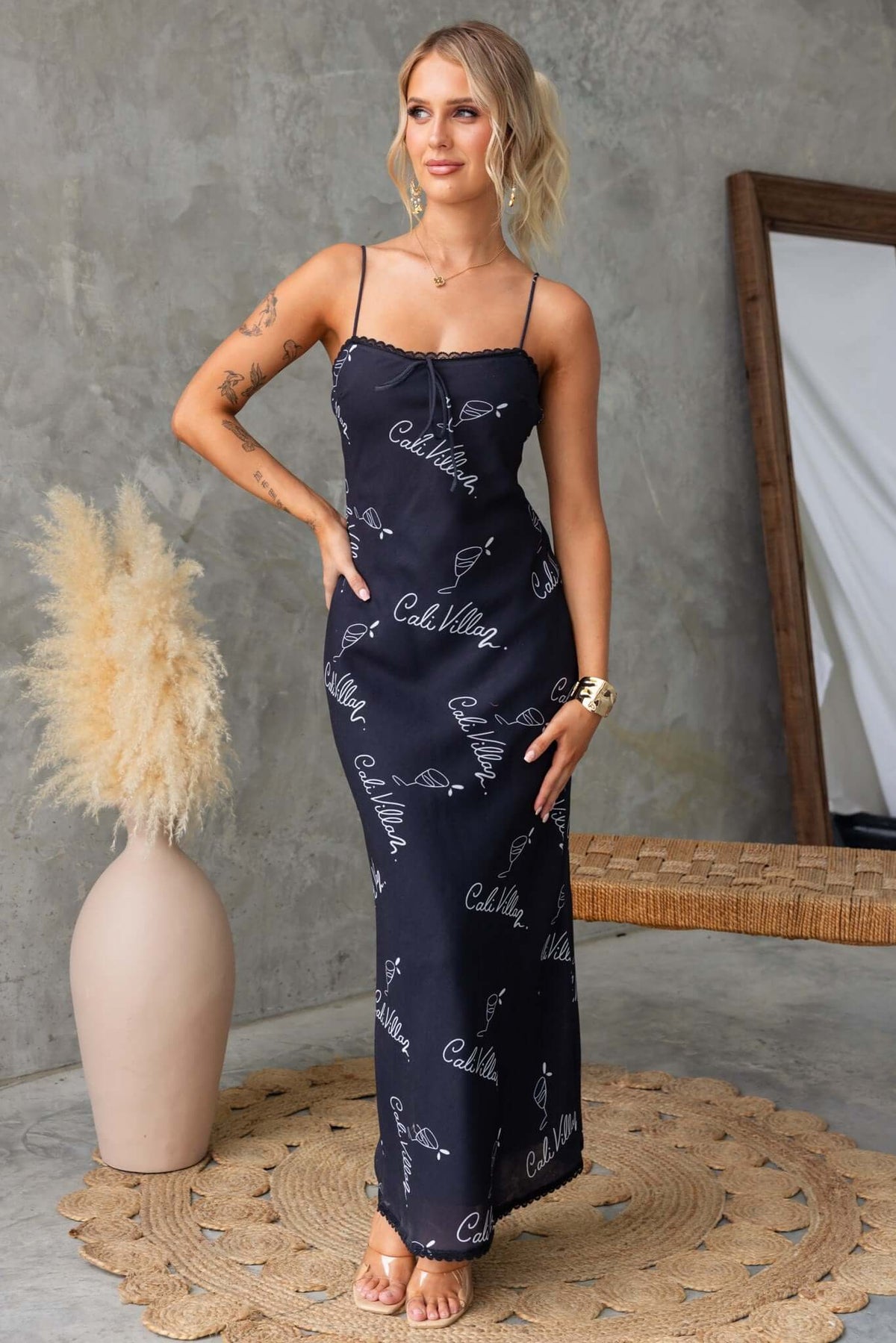 Woman wearing a black Dolomite maxi dress with adjustable straps and tie detail in a stylish indoor setting.