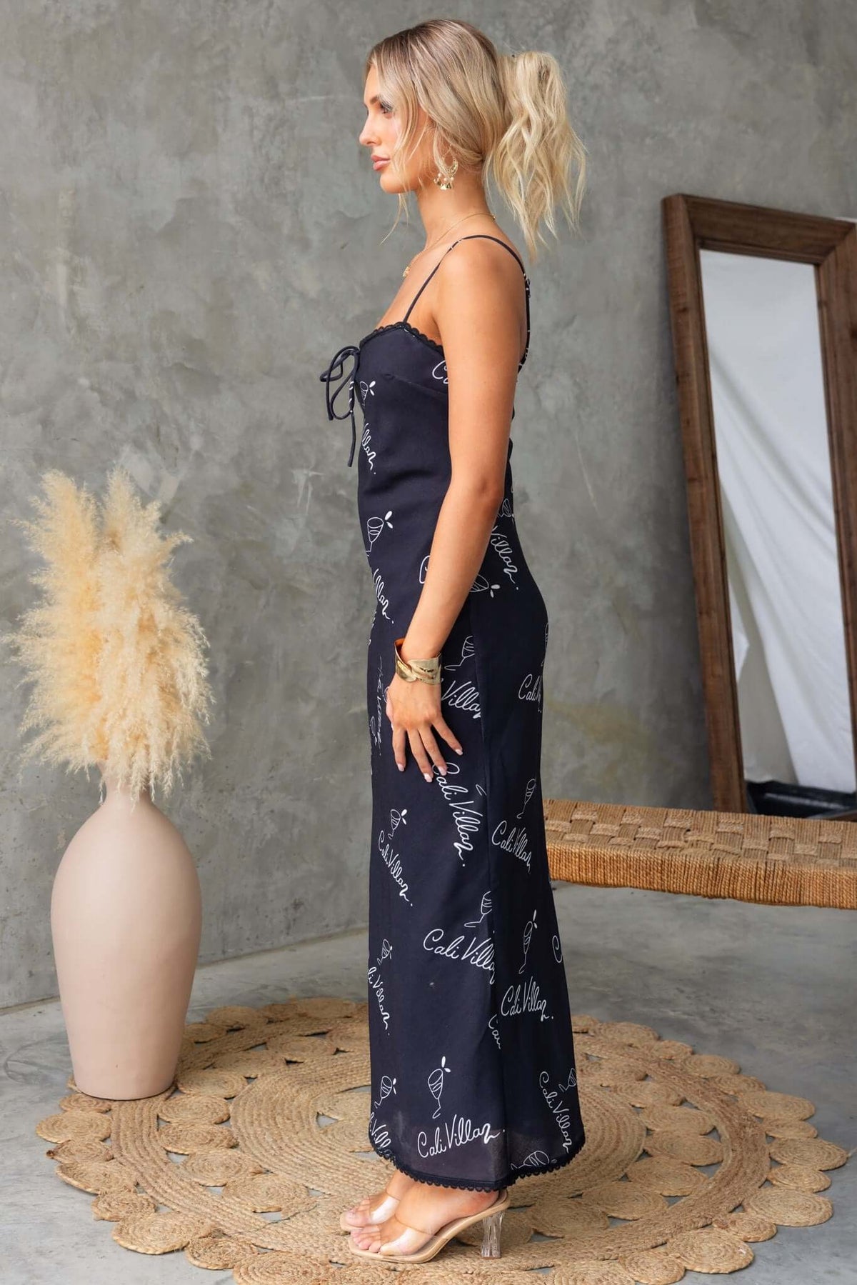 Side view of a woman wearing a black Dolomite maxi dress with adjustable straps and tie detail, showcasing a stylish silhouette.