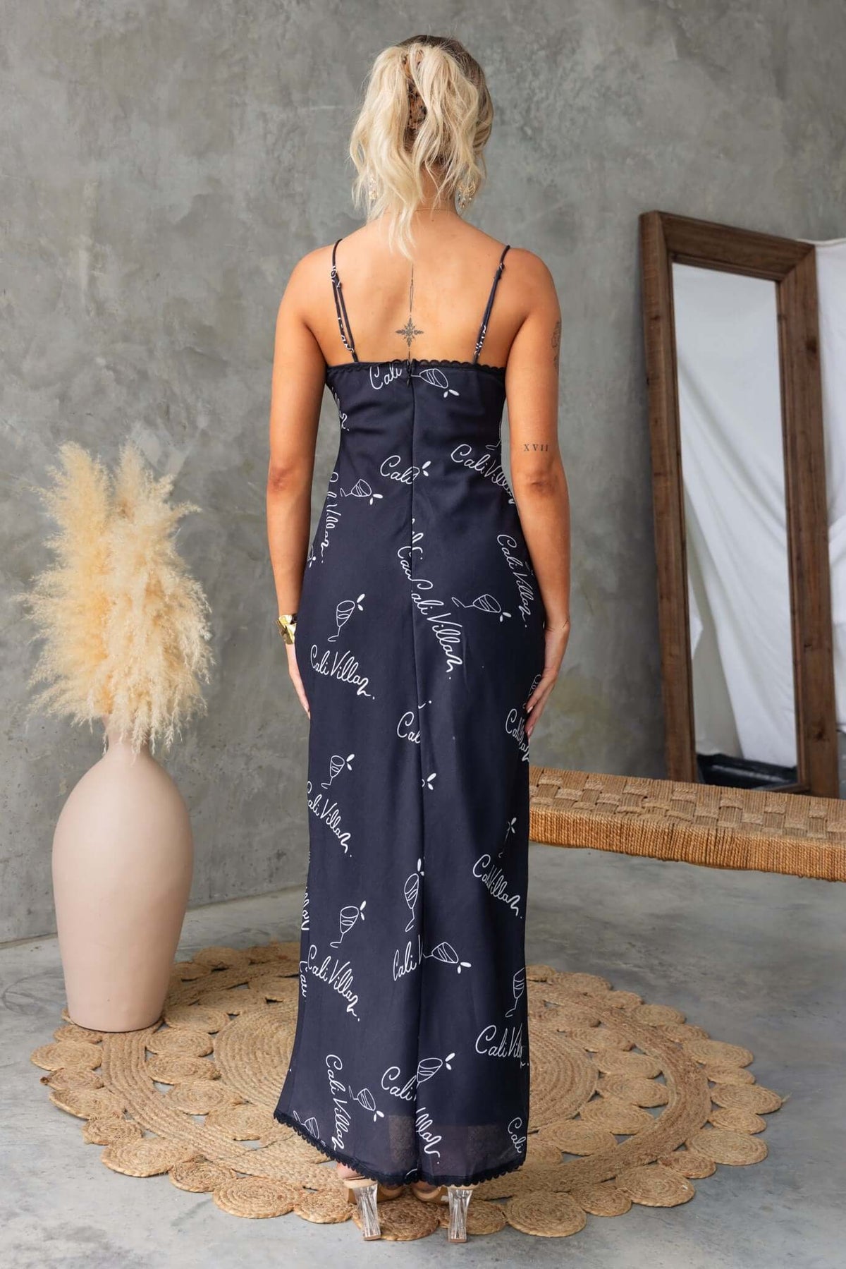 Back view of a black Dolomite maxi dress with adjustable straps and patterned detailing, styled with minimalist decor.