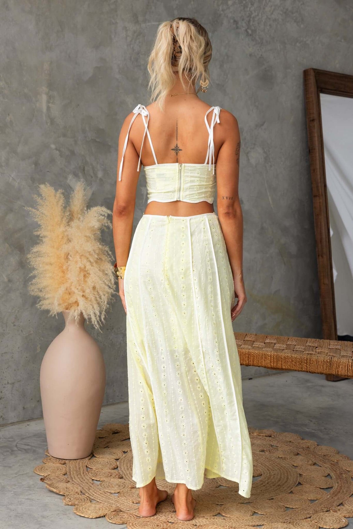 Back view of a woman wearing a non-stretch Anglaise maxi skirt and tie-strap top in soft yellow color.