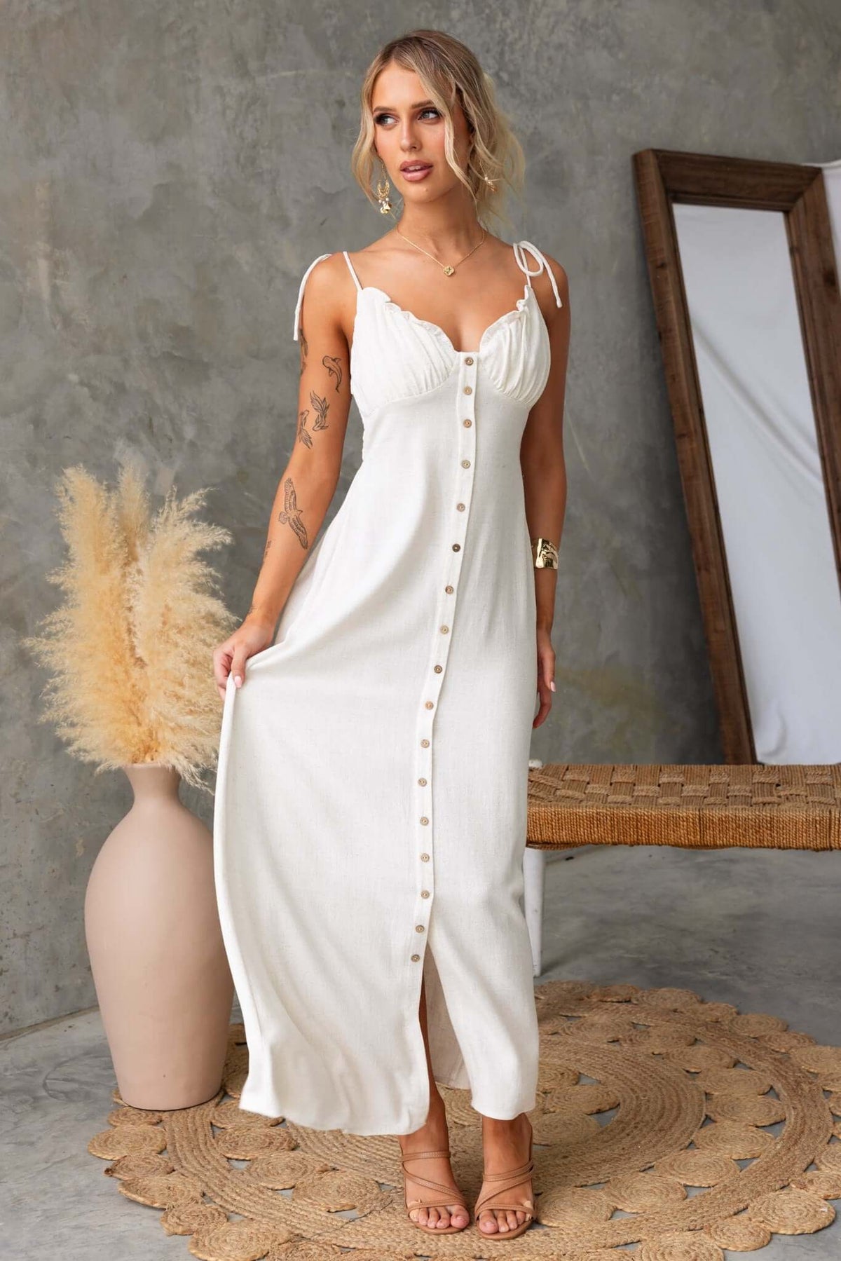 Model wearing a white Damico Maxi Dress with tie straps, faux buttons, and a front split in a stylish interior setting.