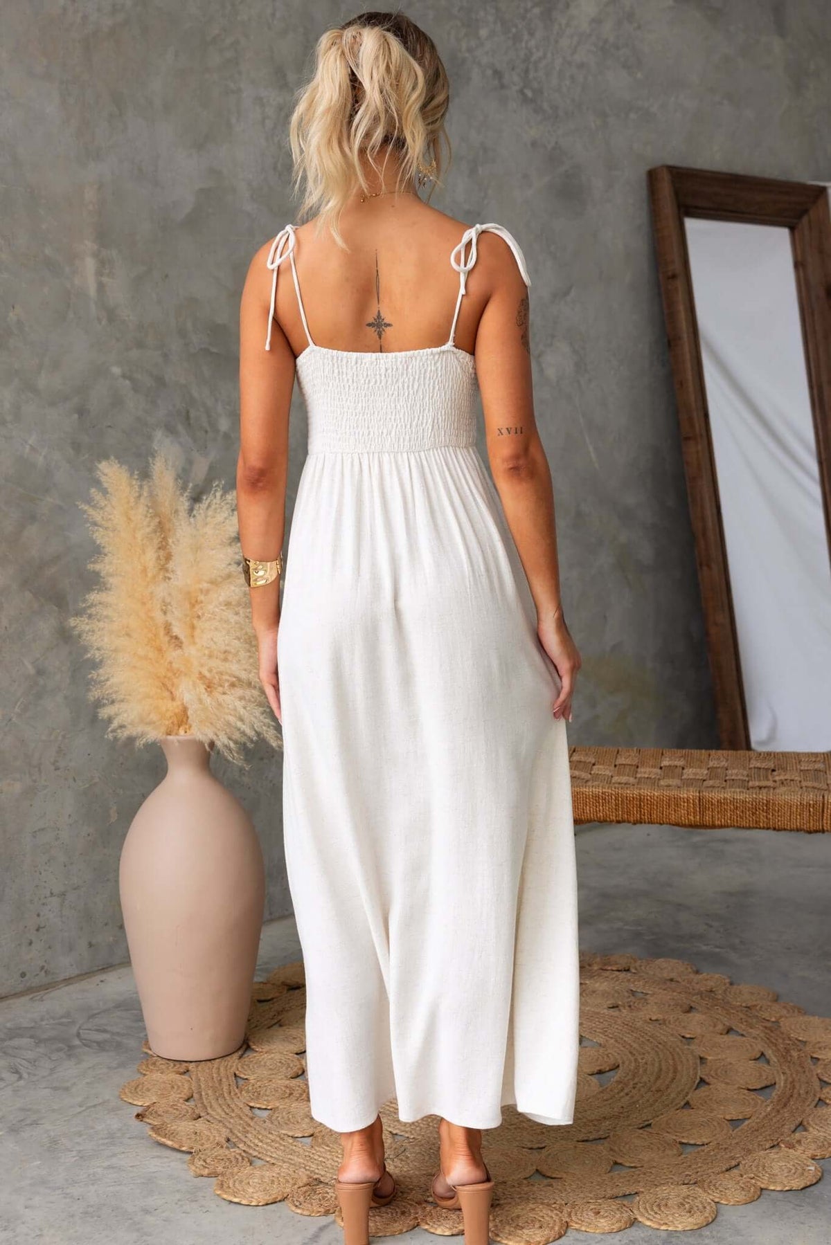 Back view of a woman in a Damico Maxi Dress with tie straps and a flowing design against a stylish interior.