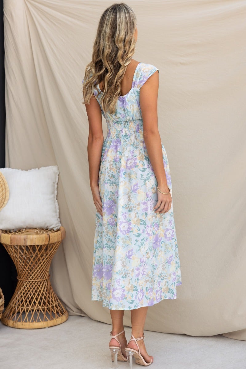 Back view of a floral print midi dress with tie detail and elastic waistband, styled with strappy heels.