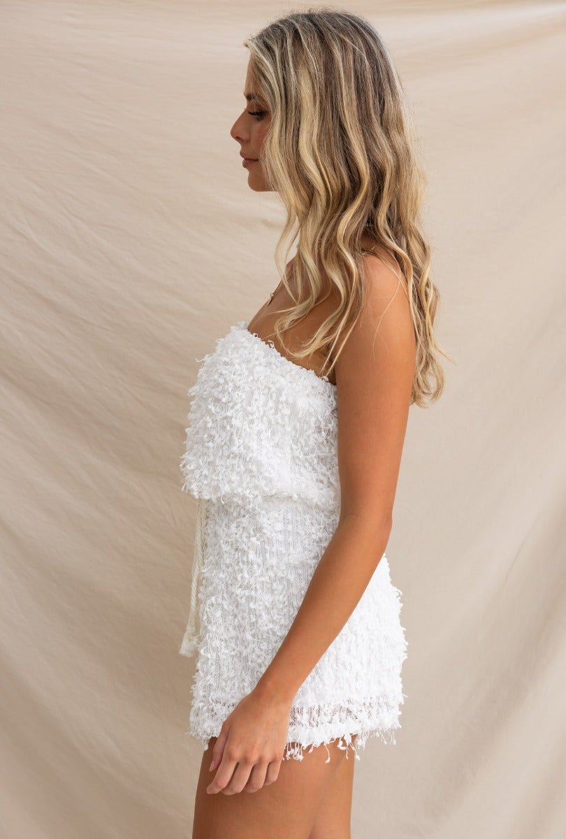 Model wearing a strapless white textured Zoey playsuit with adjustable drawstring at waist in a side profile.