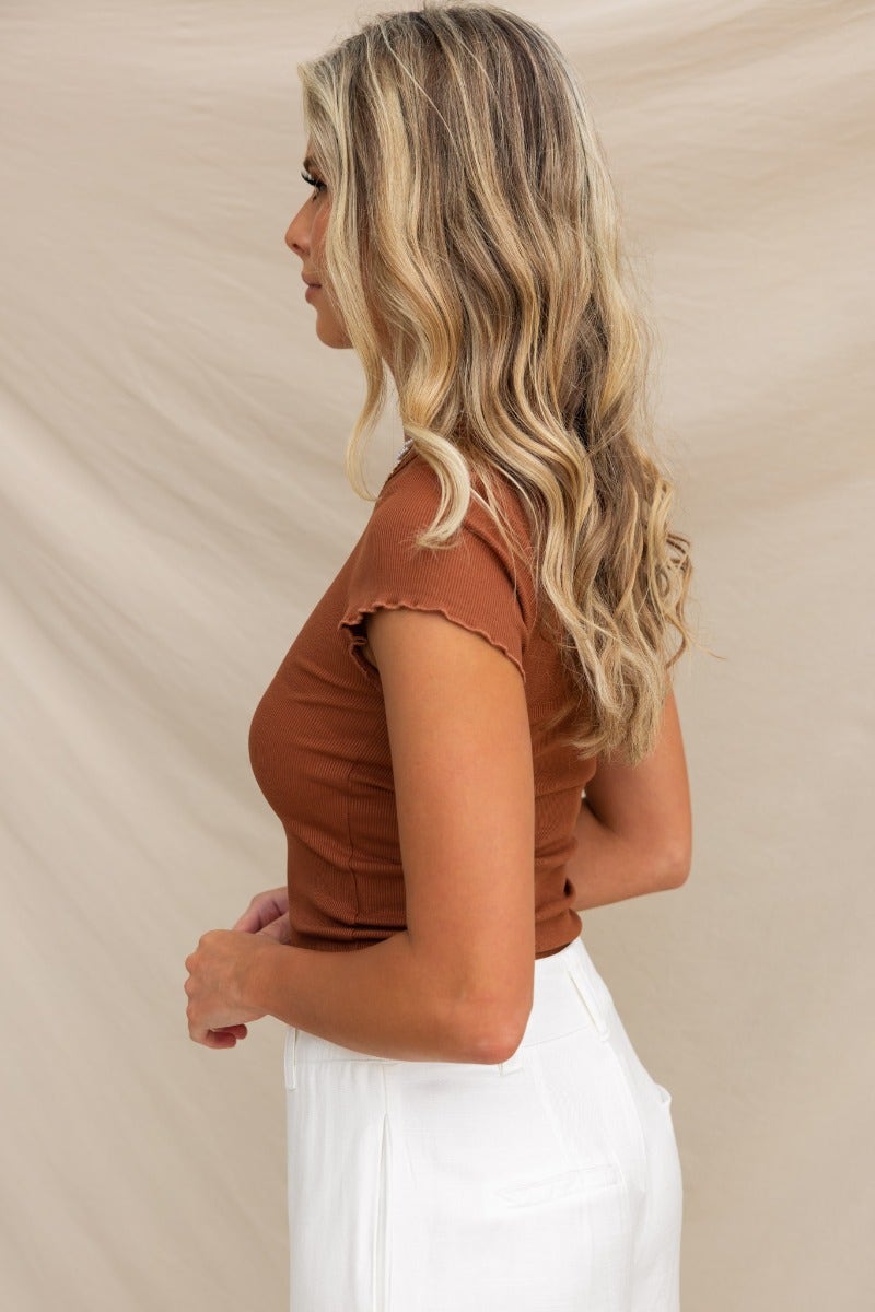 Vinny Top in rust with round neckline and frill trim sleeves, styled with white pants.