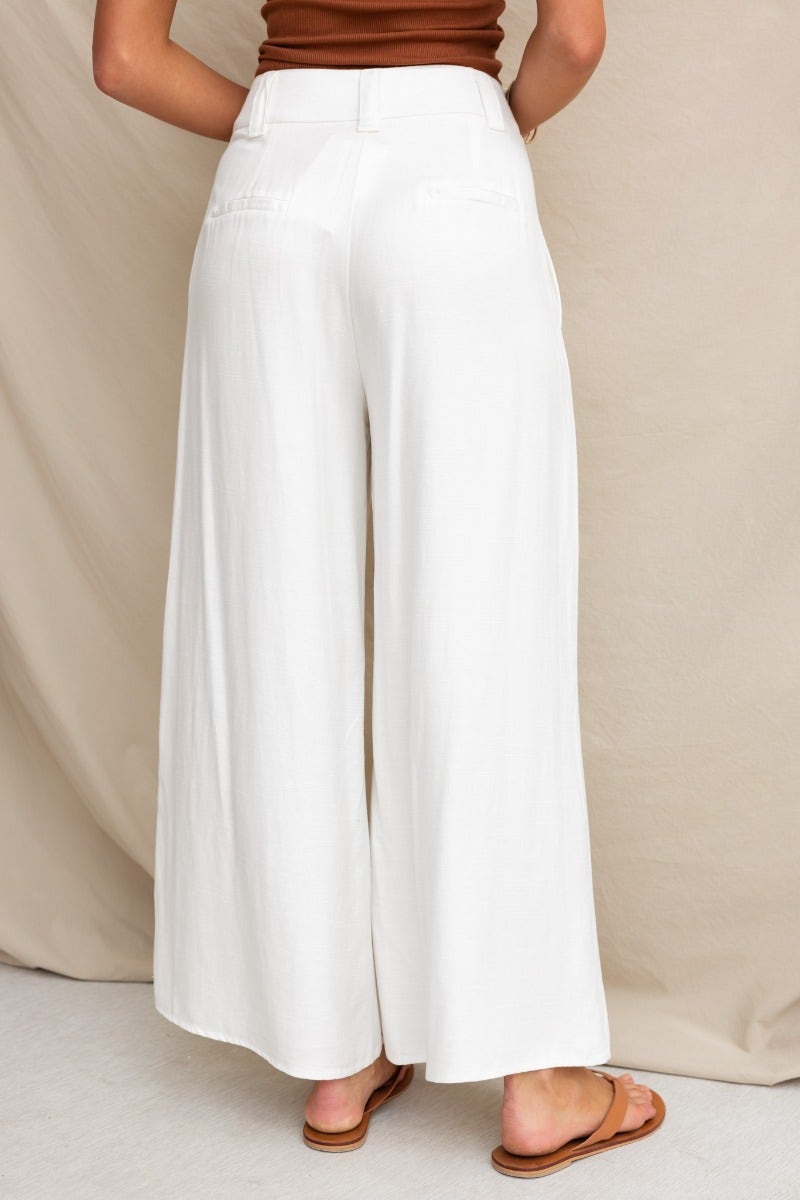 Model wearing white wide-leg silk blend pants with mid-high waist and pockets, viewed from the back.