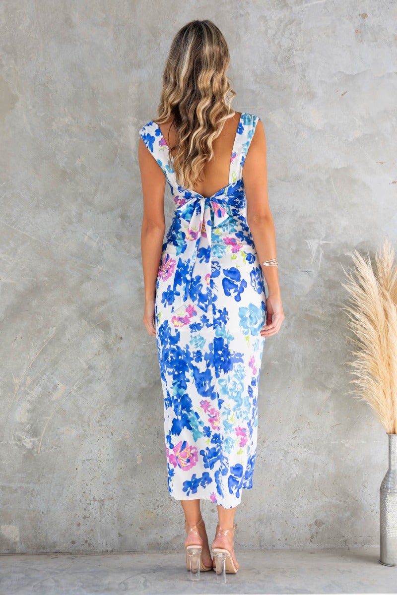 Back view of a woman wearing a floral print glistening maxi dress with a cowl neckline and tie at the back.