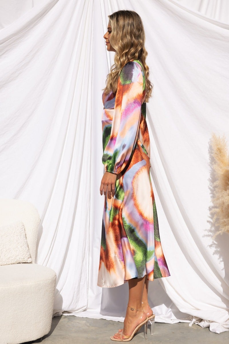 Model wearing a colorful satin midi dress with a V-neckline and cut-out detail, styled with heels.