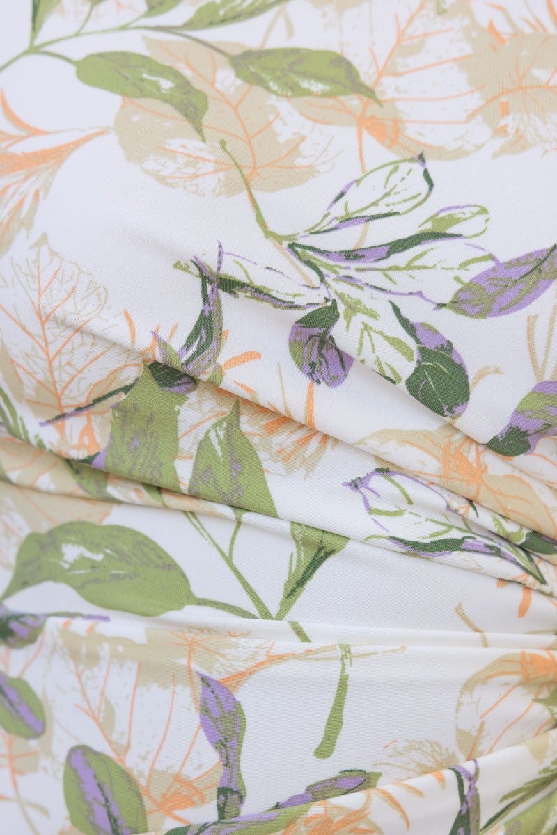 Close-up of floral print fabric featuring green and purple leaves on a soft white background.
