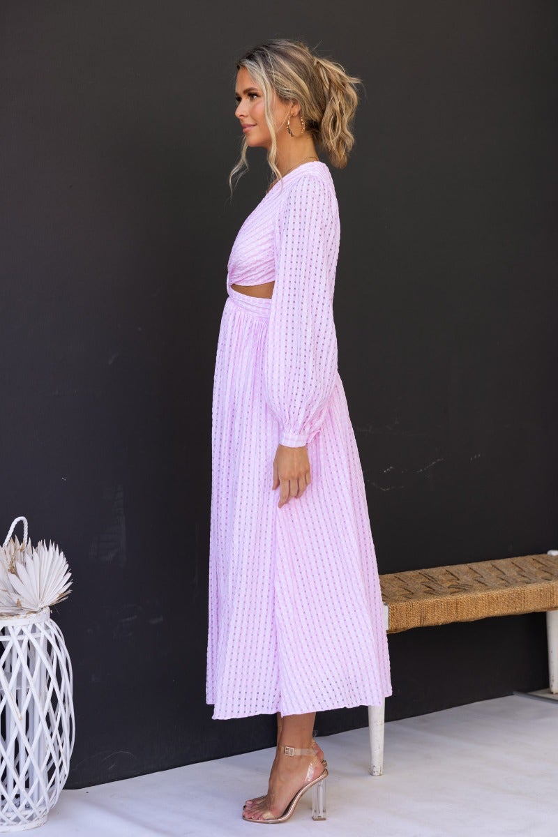 Side view of a model in a pink textured Devine Maxi Dress featuring an open plunge neckline and cut-out waist.