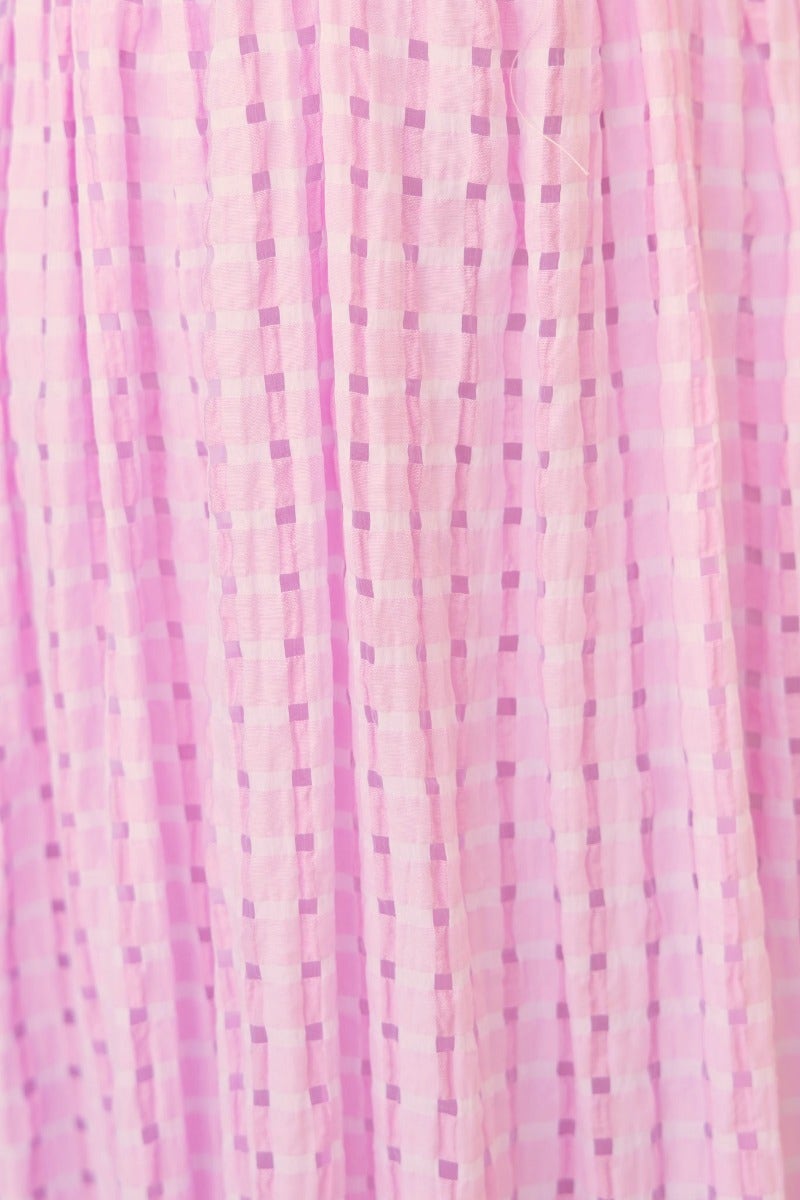 Textured pink fabric of the Devine Maxi Dress showcasing a checkered pattern and flowing material.