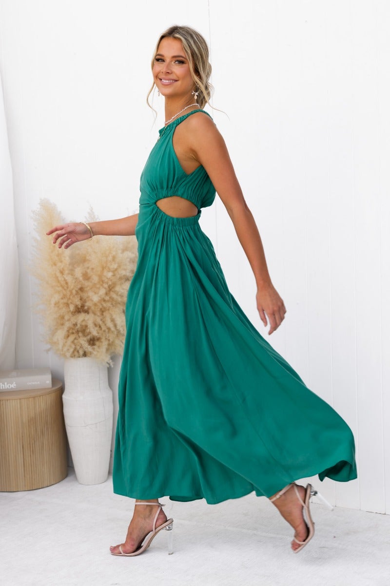 Model wearing a Silvena Maxi Dress in teal with a high neckline, cut-out waist, and flowing skirt.