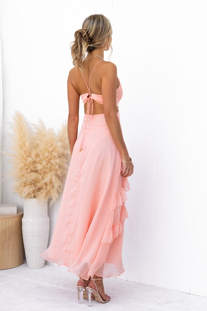 Back view of a model in a pink Blaze Maxi Dress with adjustable straps and ruffle details, styled with soft glam.